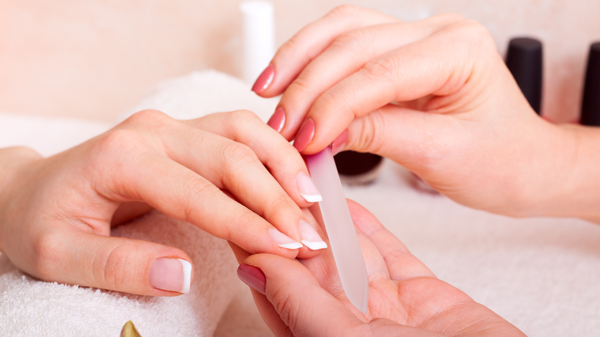 Close-up of a person receiving a manicure, with a nail technician filing their nails with a emery board.