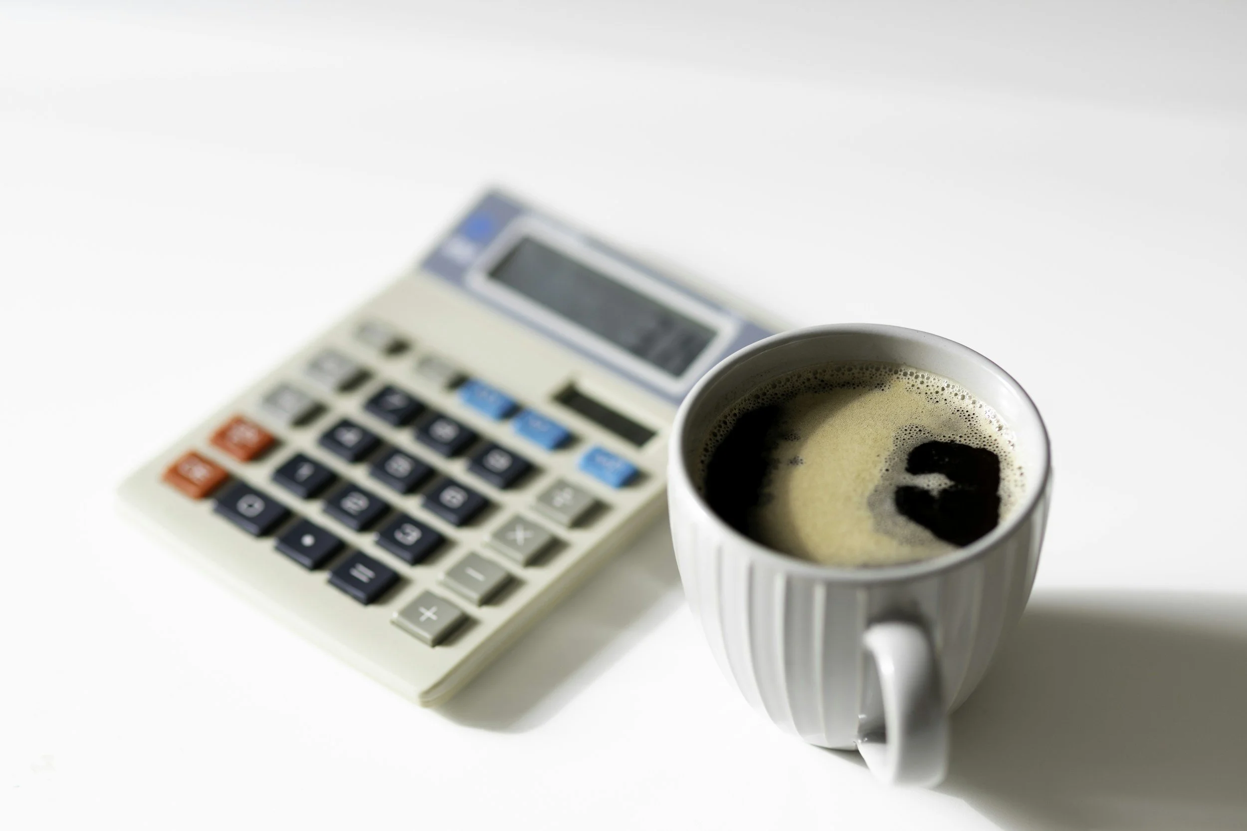 A calculator and a mug of coffee on a white surface.