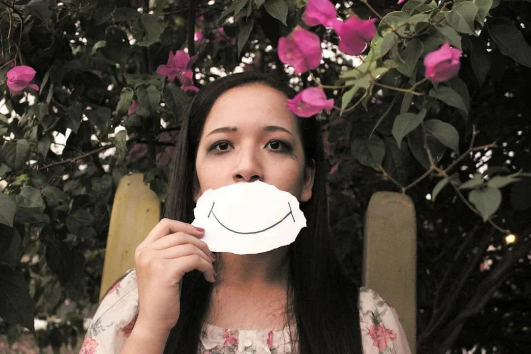 Woman holding a paper smile in front of her face while looking serious