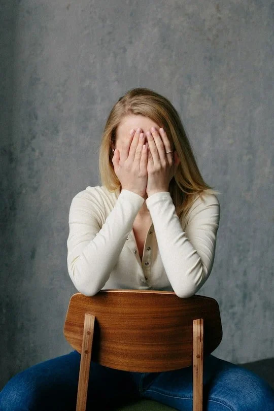 Woman sitting with her face in her hands representing the overwhelm and emotional exhaustion that leads women to seek anxiety therapy in Arizona