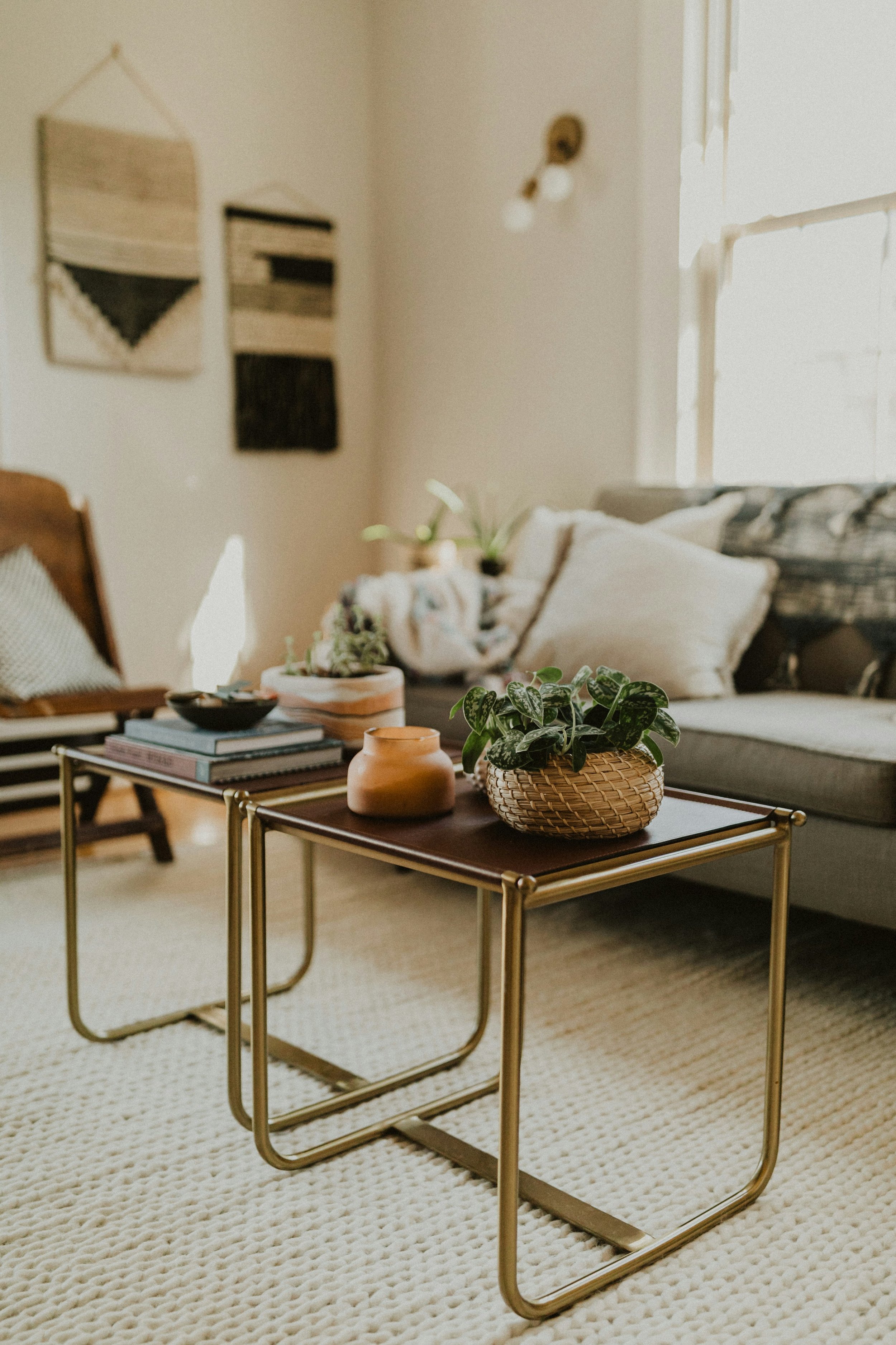 A trauma therapists office with two modern nesting coffee tables, a beige sofa with cream and patterned pillows, a wooden armchair, wall art, and natural light from windows.