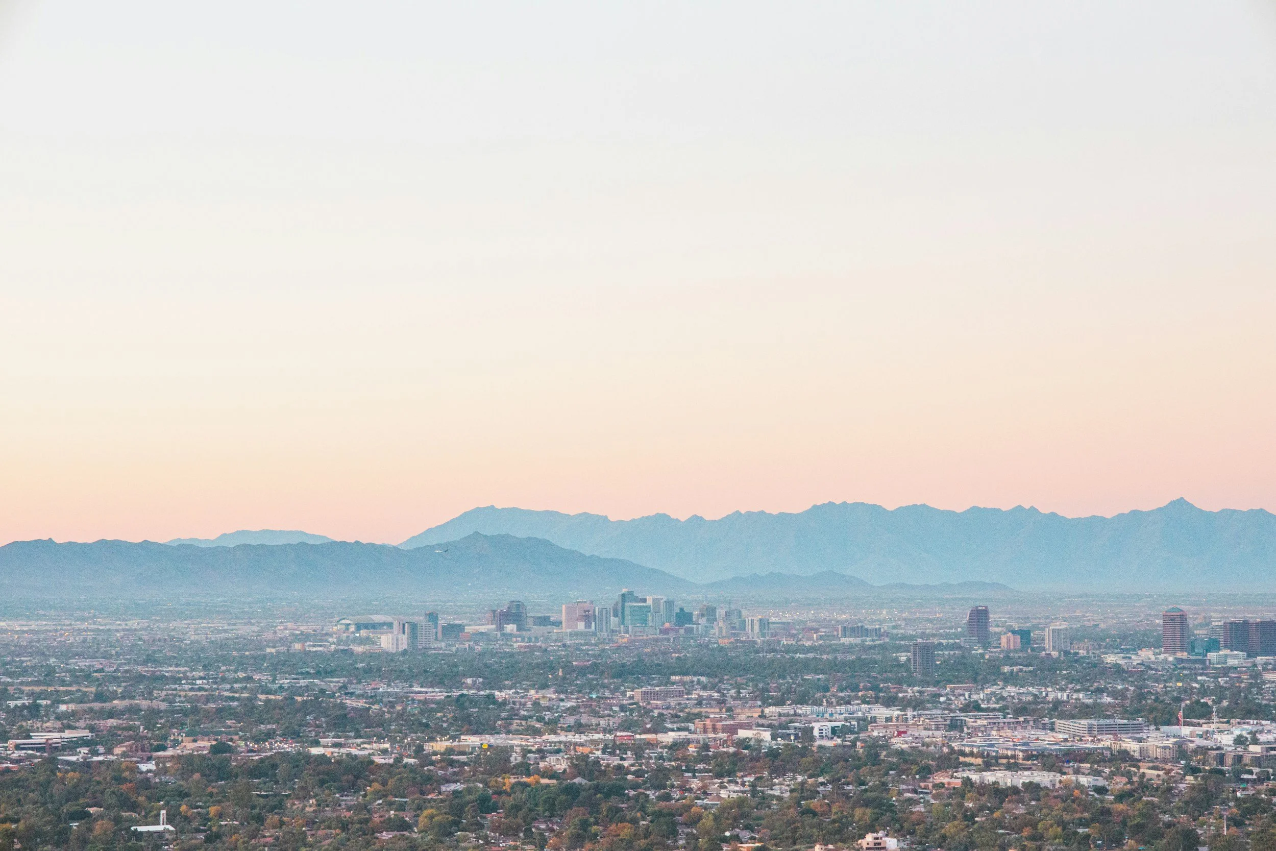 Phoenix skyline with high-rise buildings and mountain range in the background at dusk or dawn.