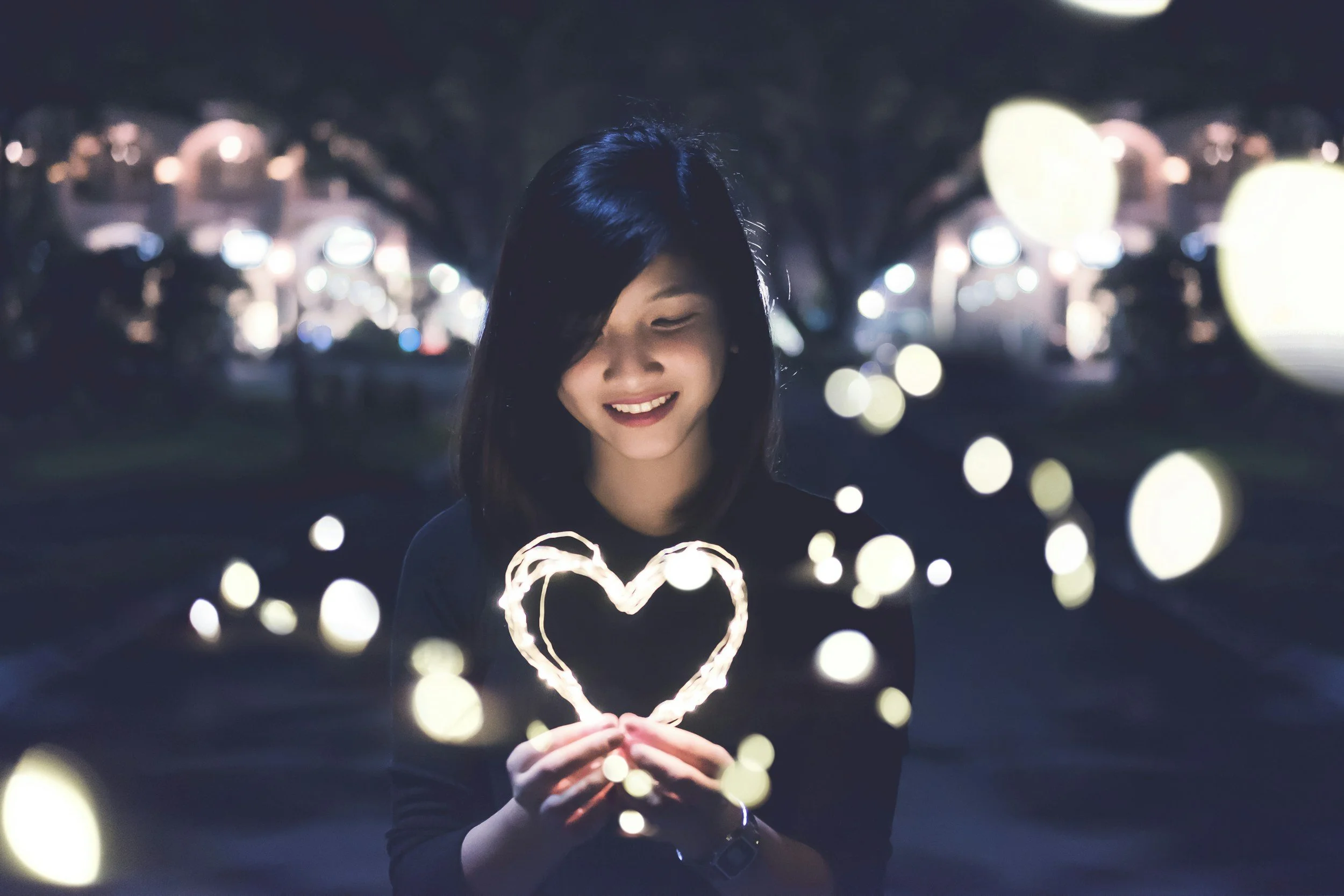 Woman smiling while holding a glowing heart representing self-love and emotional healing through anxiety therapy