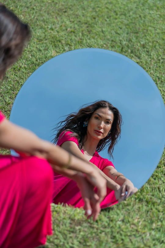 Woman gazing at her reflection in a round mirror outdoors representing self-awareness and identity through therapy for women in Arizona