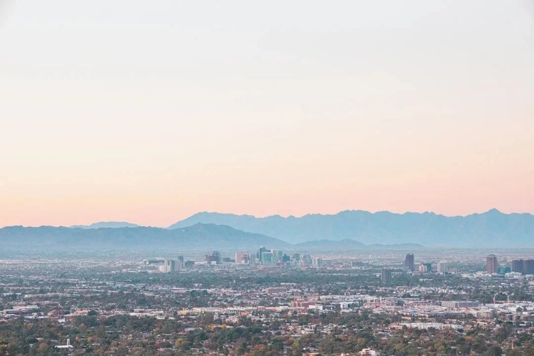 Phoenix skyline with high-rise buildings and mountain range in the background at dusk or dawn.