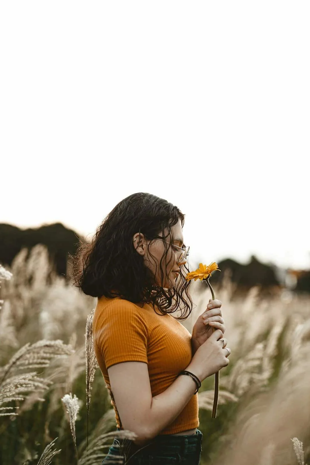 Woman pausing to smell a flower in a golden field representing mindfulness and grounding through anxiety therapy in Arizona