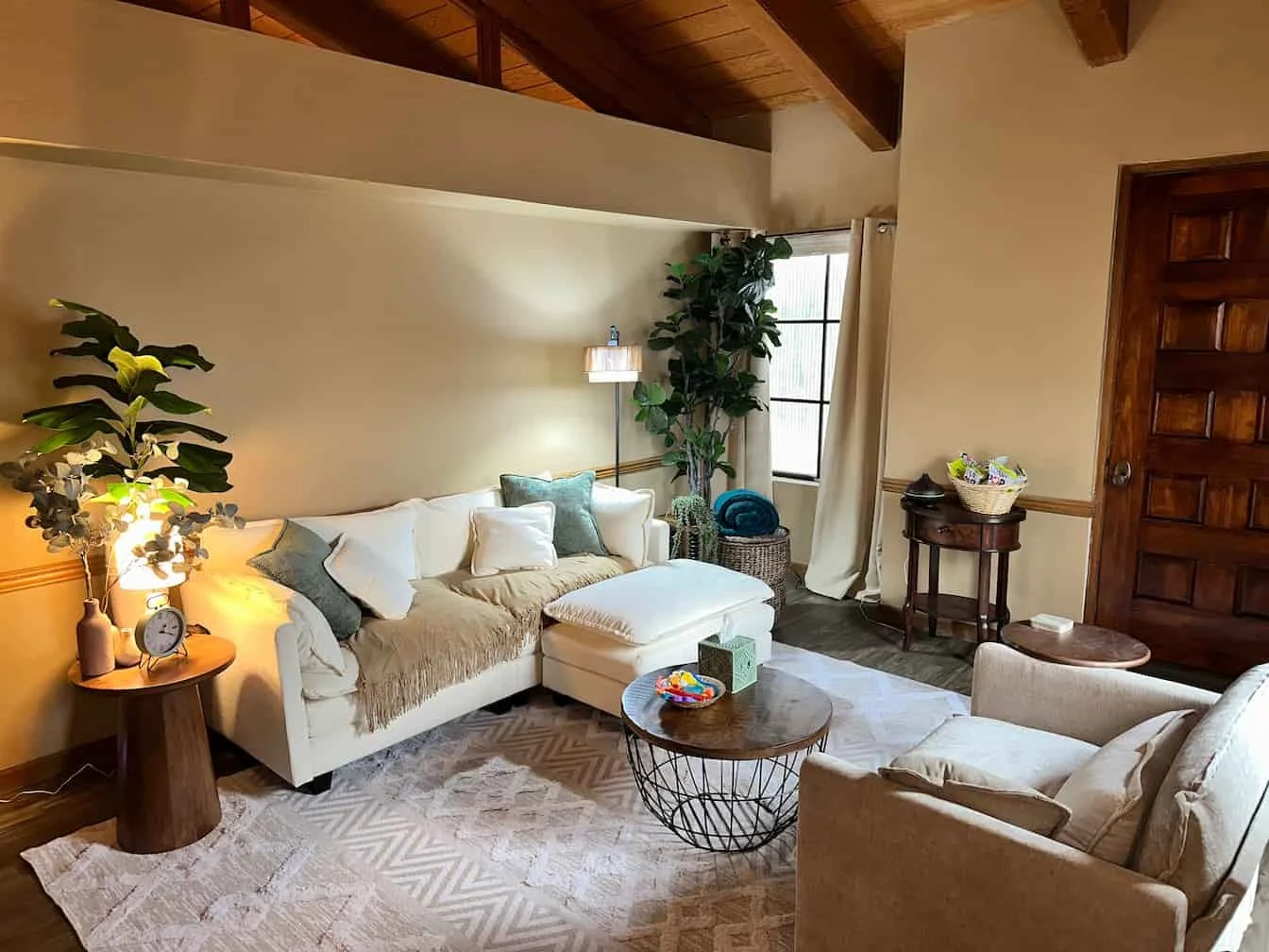 Phoenix Therapist office with beige and rust-colored sofas, a round wooden coffee table, potted plants, a framed landscape painting, a standing lamp with multiple gold-colored shades, a side table with a clock.