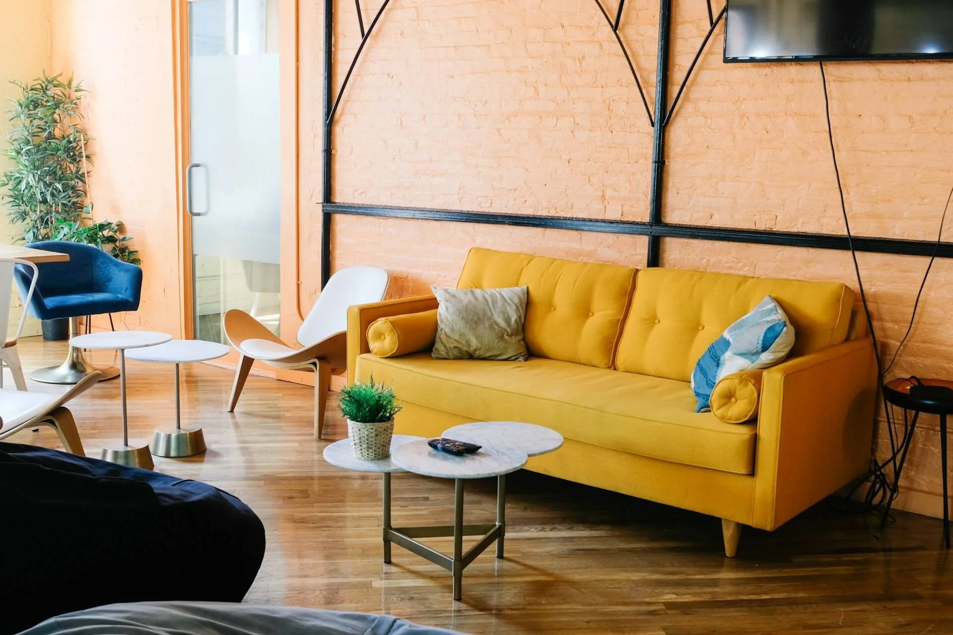 Interior of a trauma therapist in Phoenix's office with a yellow sofa, white and blue pillows, a small marble coffee table, a green plant, and a flat-screen TV mounted on the wall. The office of a Phoenix Therapist