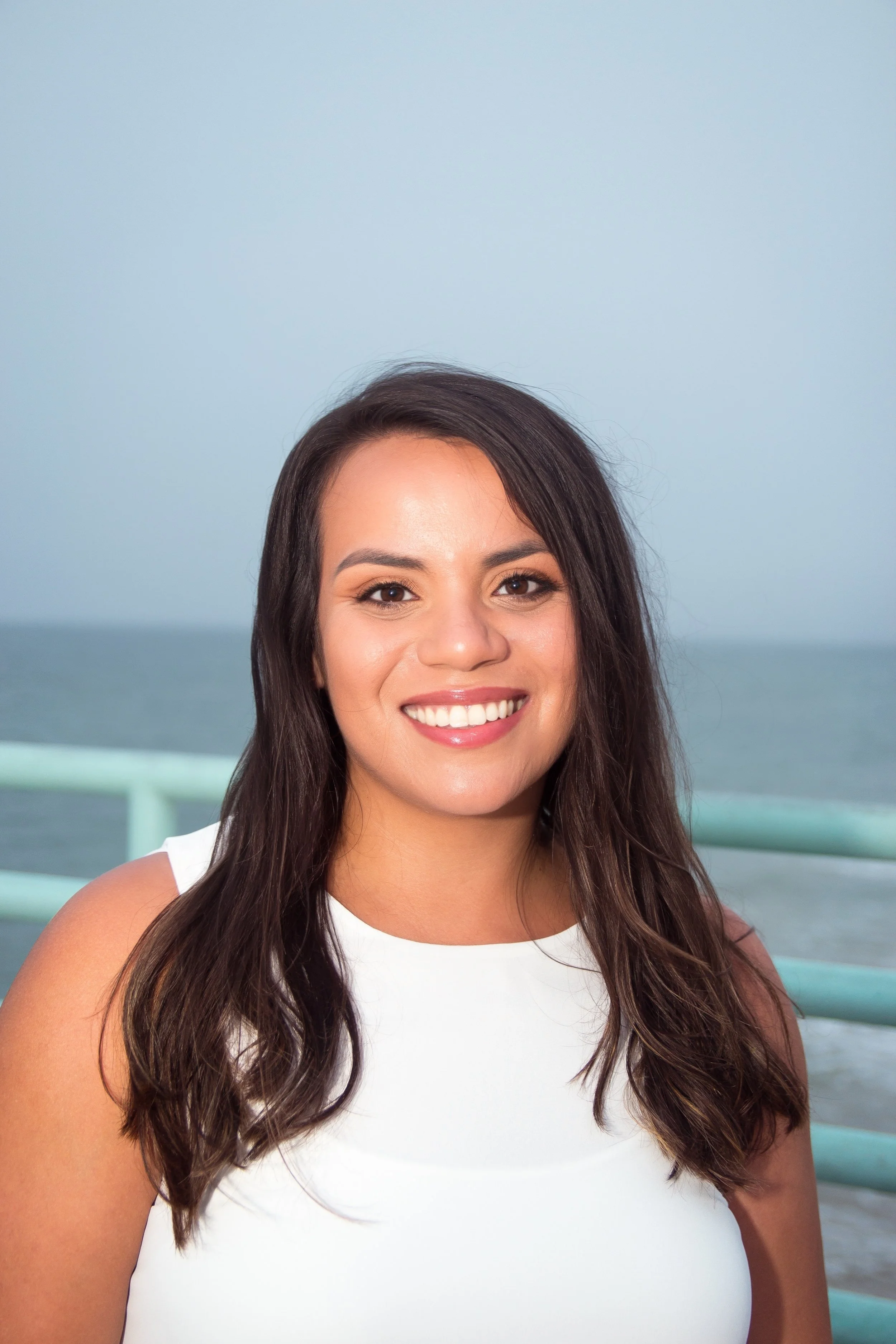 A young woman with long dark hair, smiling on a boat with the ocean in the background. A Phoenix Trauma therapist.
