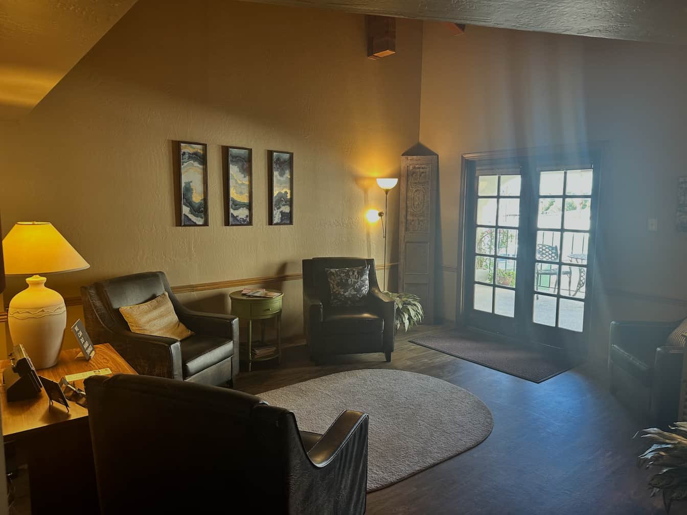 Waiting area for a Phoenix therapy office with eight wooden chairs with striped cushions arranged around a round coffee table on a colorful patterned rug. There are plants near the windows and artwork on the wall/