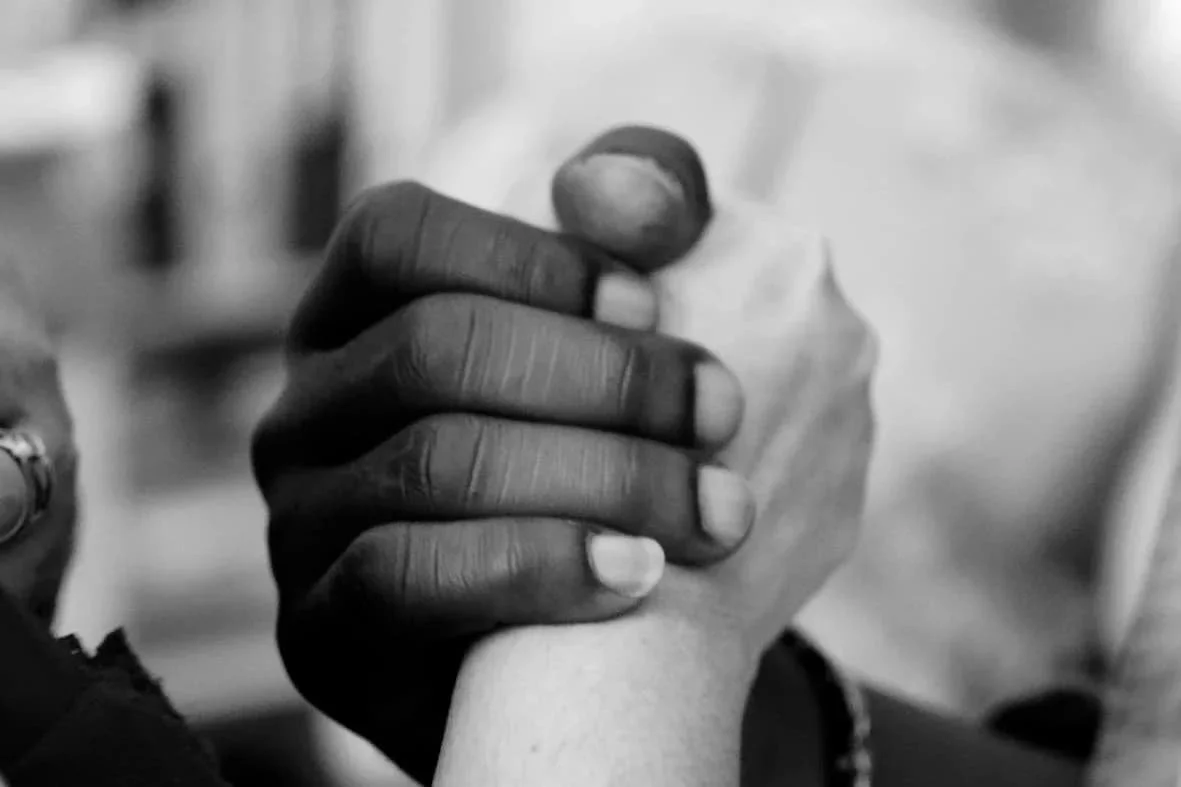 Two hands clasped together in black and white representing support, trust, and connection through trauma-informed therapy in Arizona