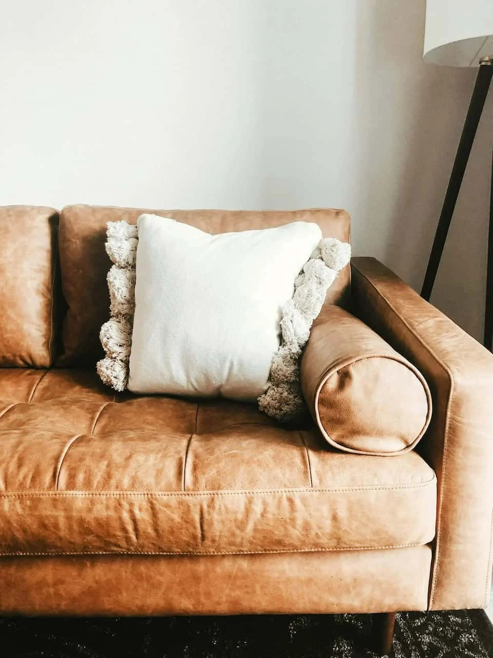 A brown leather sofa in a EMDR therapist's office with tufted cushions, a white pillow with fringed edges, and a black floor lamp in the background.