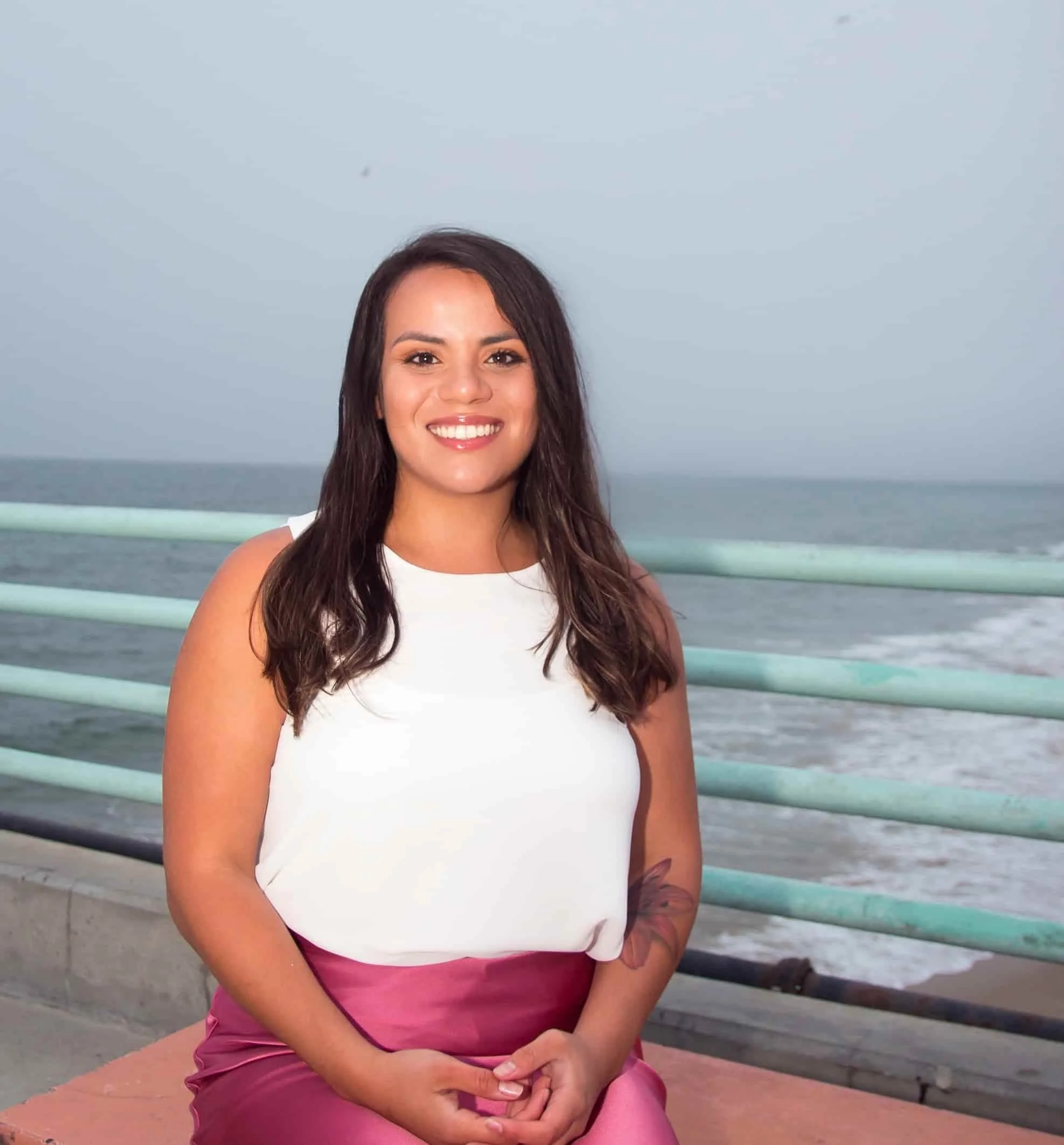Trauma therapist smiling and seated outdoors by the ocean, welcoming and approachable
