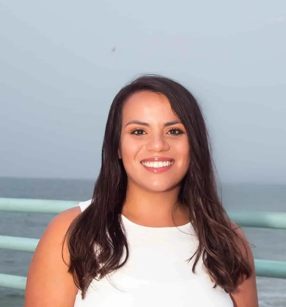 A Trauma therapist with long dark hair, smiling on a boat with the ocean in the background.