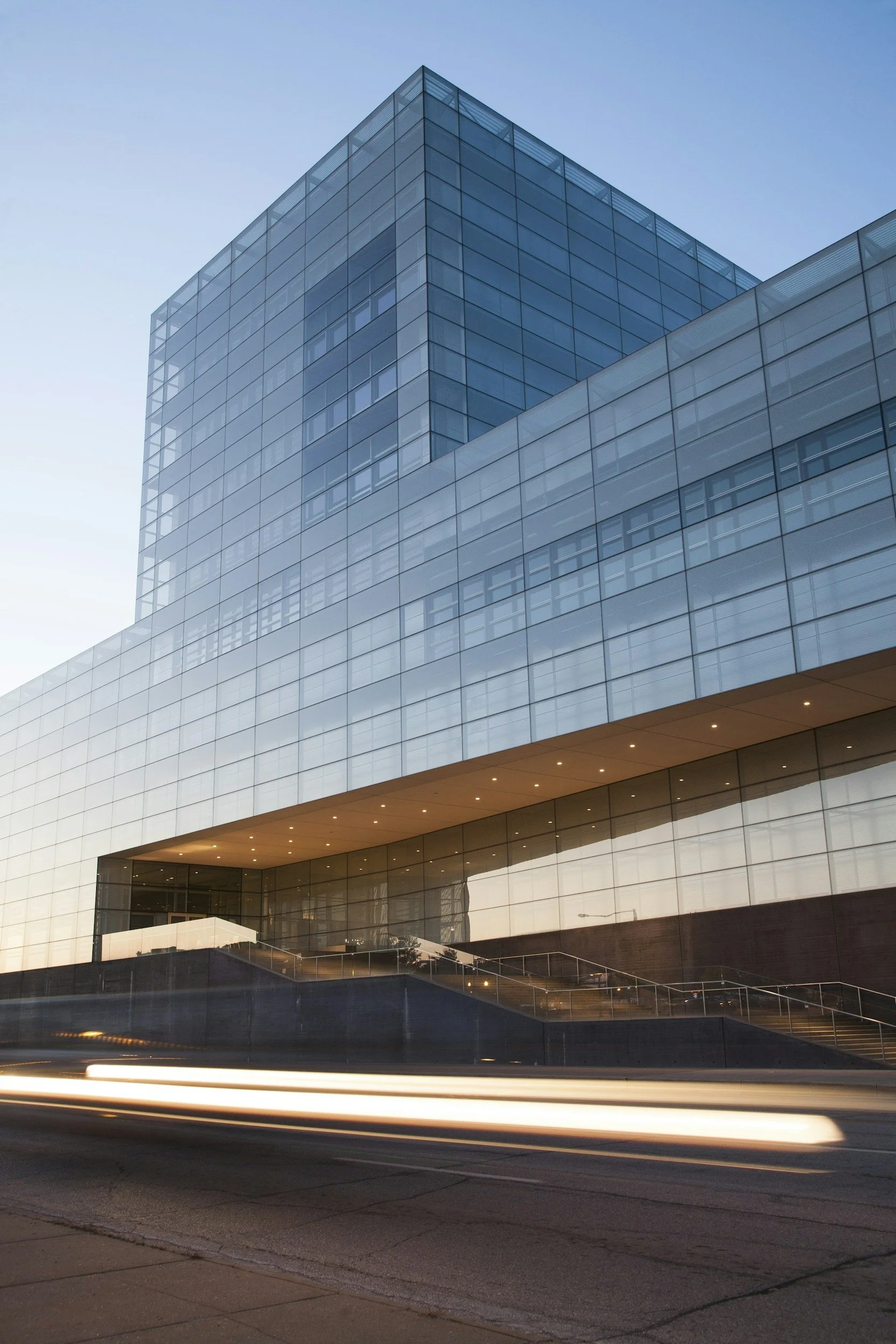 Modern glass office building during sunset with light streaks from moving vehicles in the foreground.
