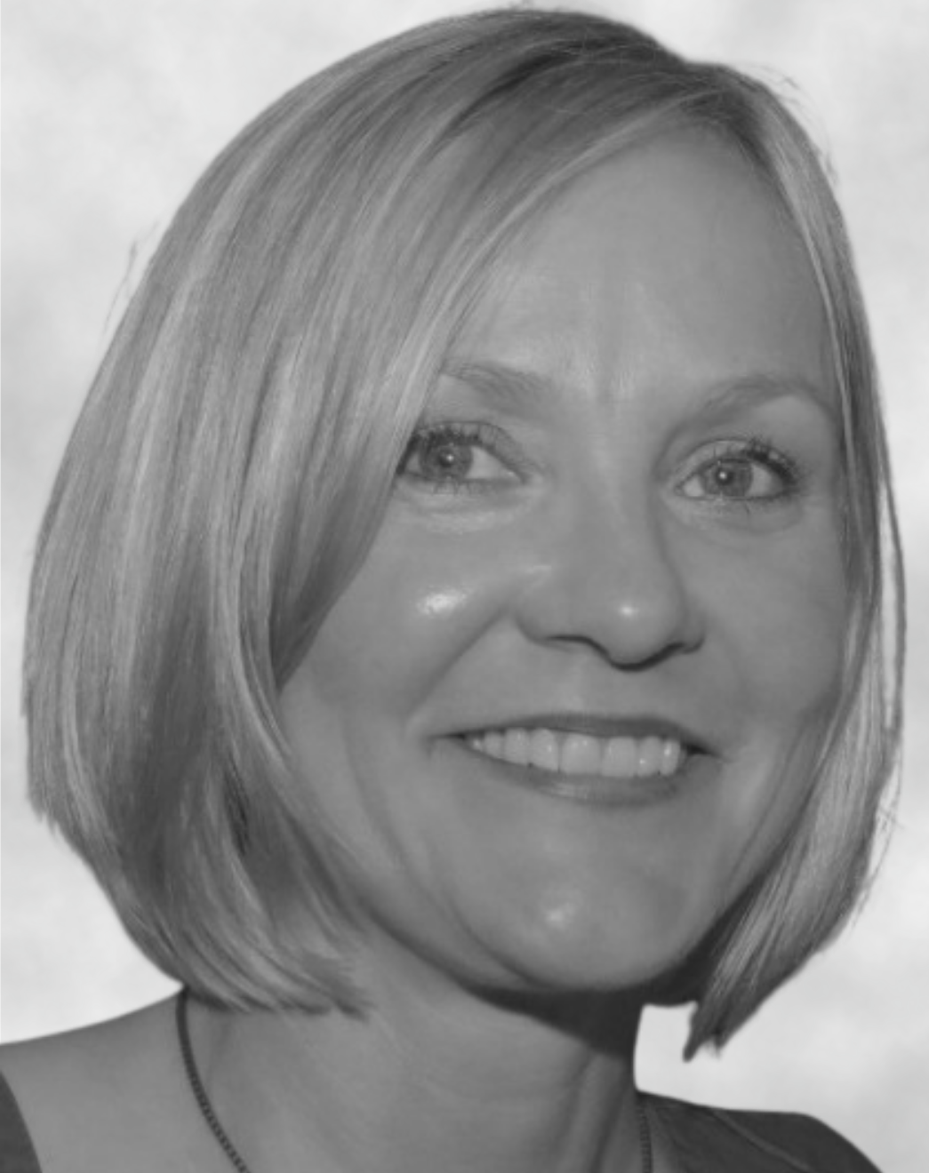 Black and white portrait of a woman with shoulder-length straight hair, smiling, wearing a necklace.