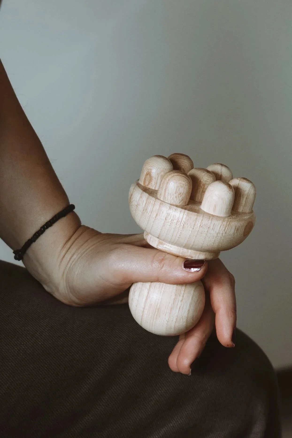 Main tenant une cloche en bois naturelle, conçue pour jouer ou comme décoration, dans un cadre intérieur avec un fond neutre.