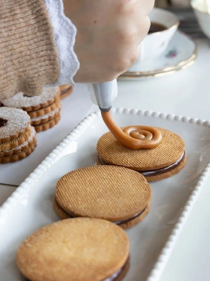 Une personne décore des biscuits avec du caramel mousseline à l'aide d'une poche à douille.