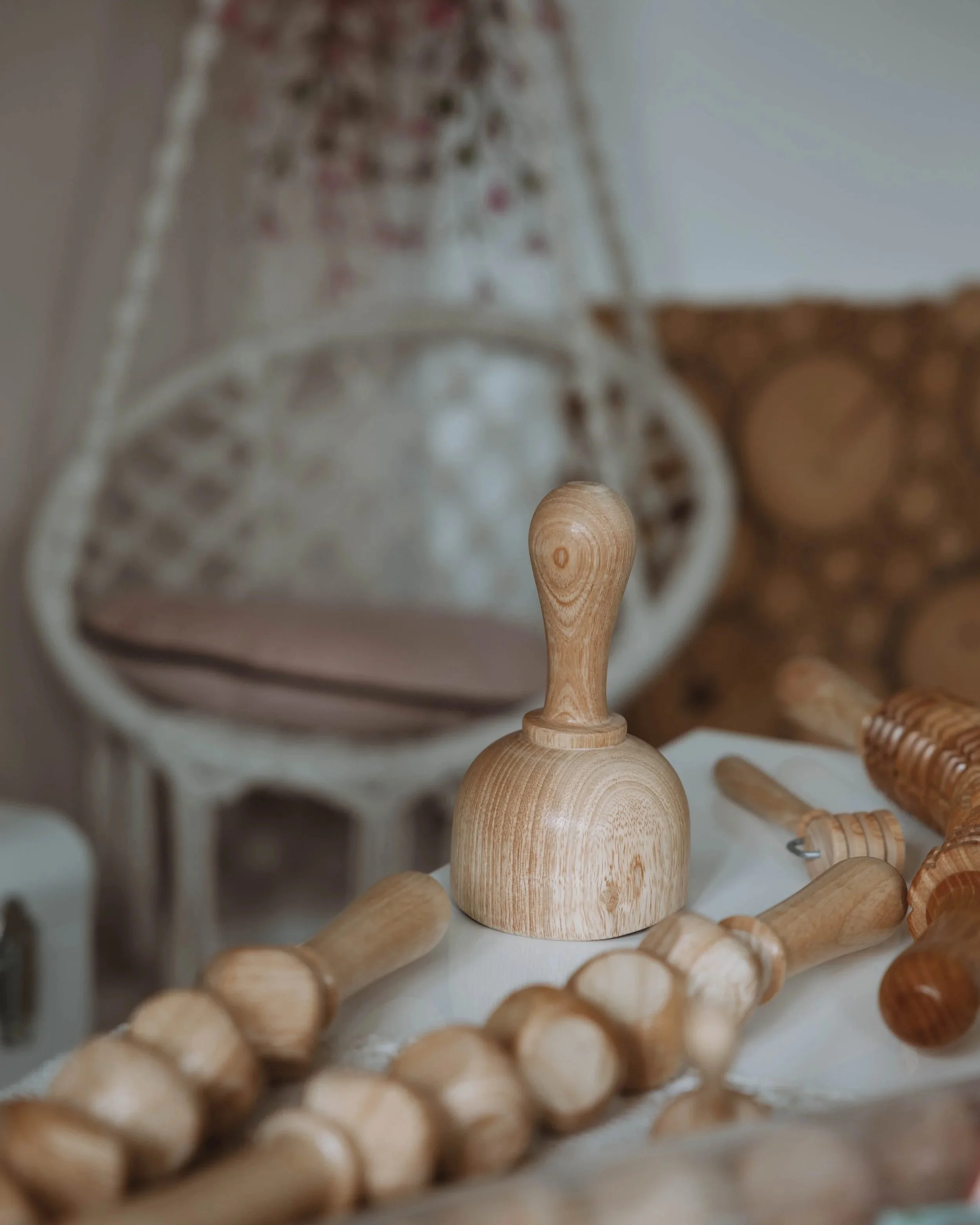 Objets en bois, y compris un maillet et des rouleaux, sur une surface, avec un fauteuil en osier flou en arrière-plan.