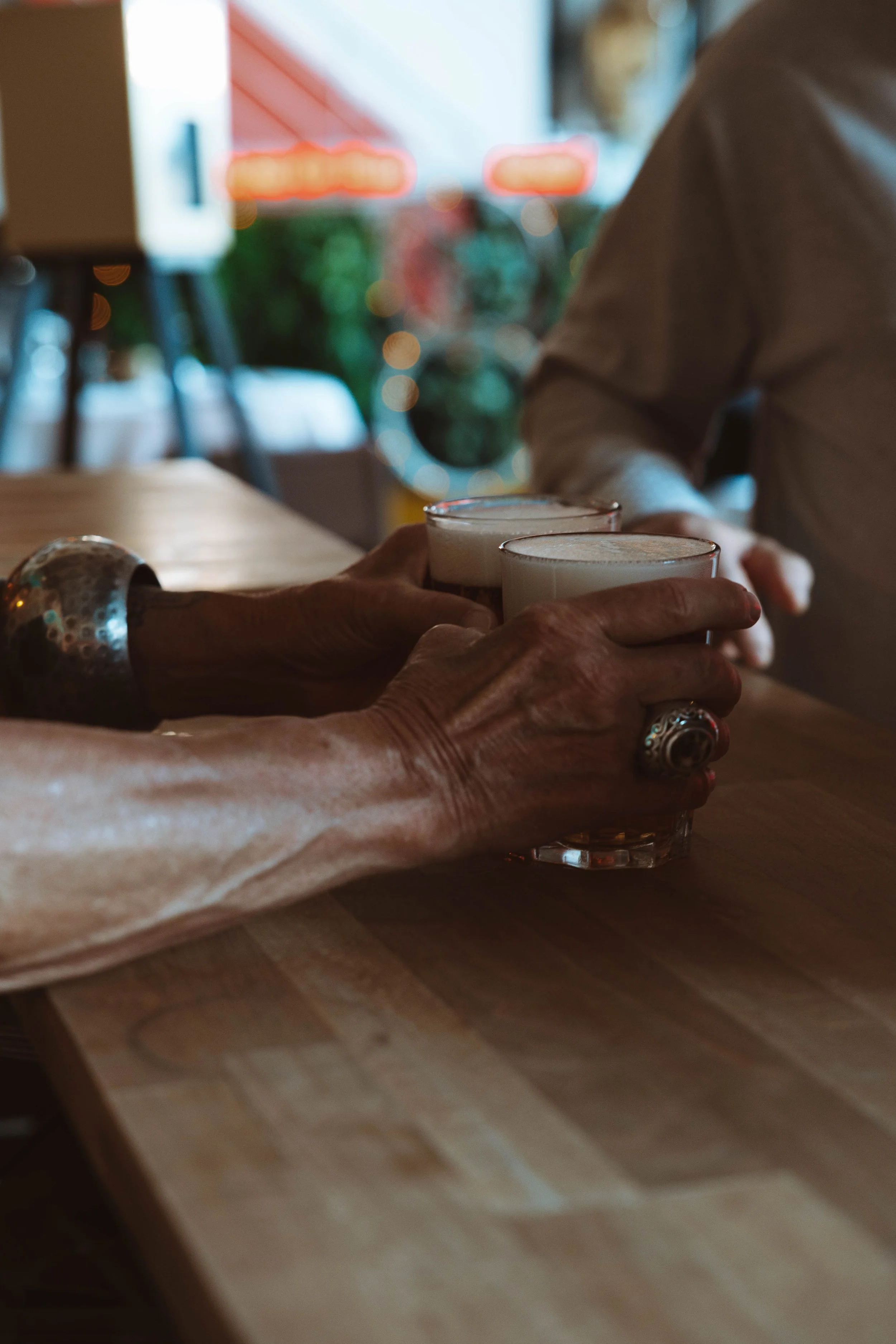 Trois personnes se serrent la main tout en tenant des verres contenant des boissons laiteuses lors d'une rencontre dans un café ou un restaurant, avec un fond flou de décor intérieur et lumière naturelle.