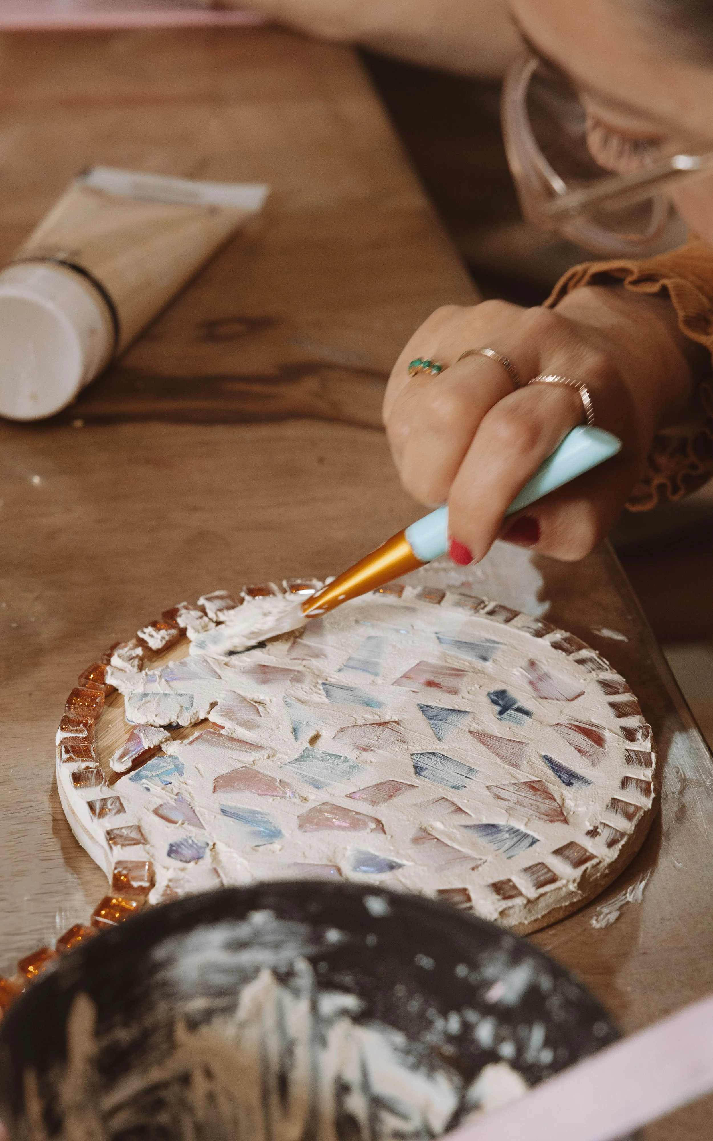 Une personne utilise un pinceau pour appliquer de la colle sur une mosaïque de céramique colorée sur une surface en bois.