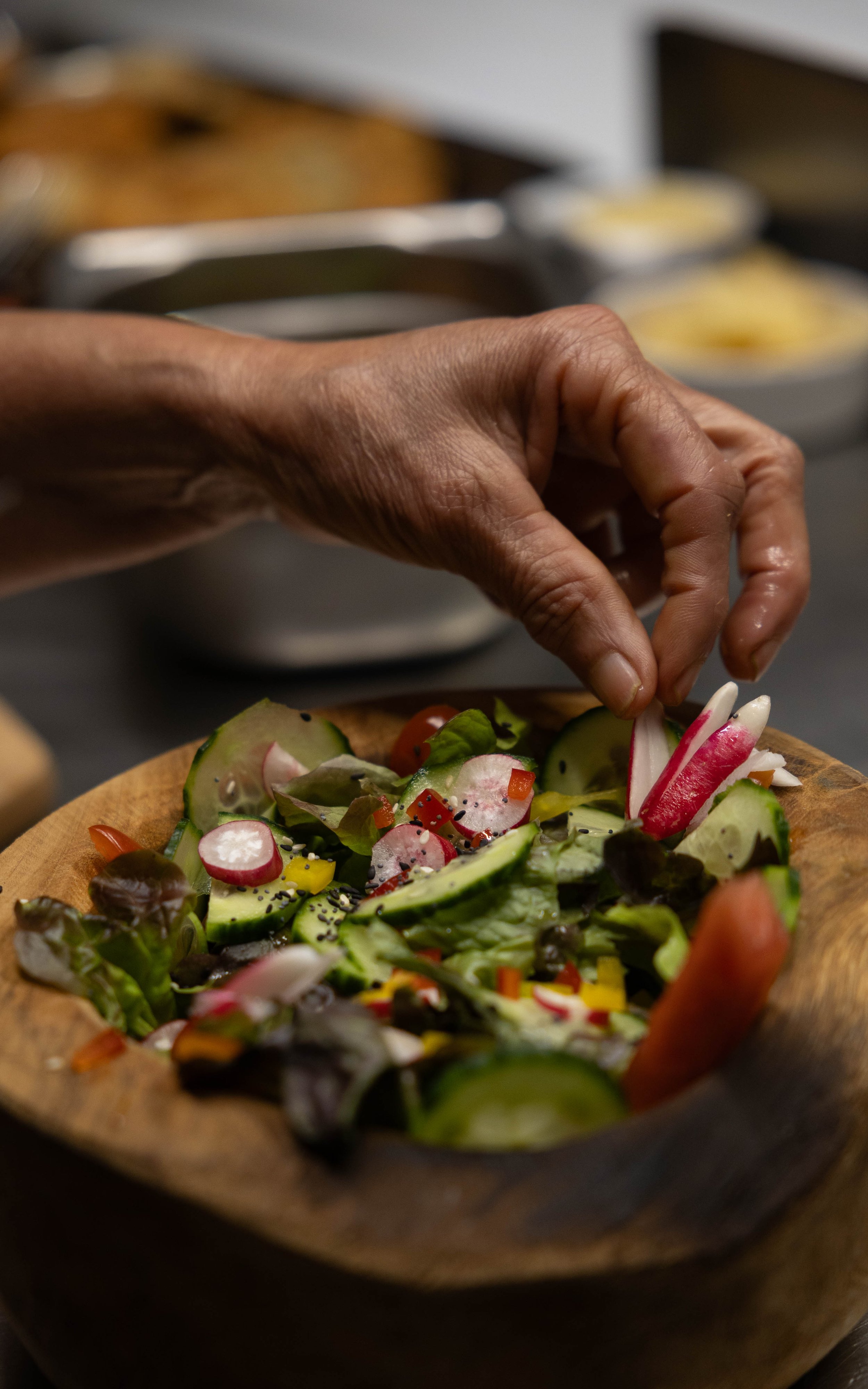 Une main qui dépose des légumes frais dans une salade dans un bol en bois.
