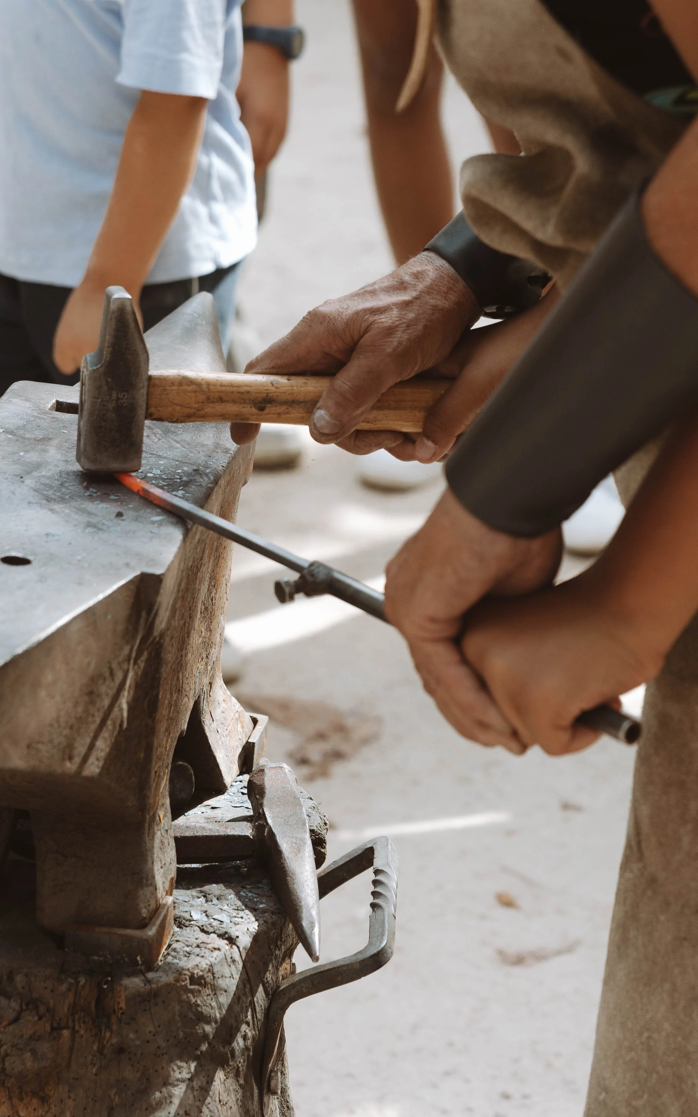 Des personnes utilisant un marteau et un fer à chaud sur un gros morceau de métal pour travailler ensemble.