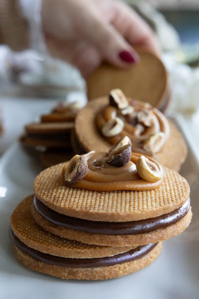 Biscuits sablés avec du chocolat et du caramel, garnis de noix, en rangée sur une assiette.