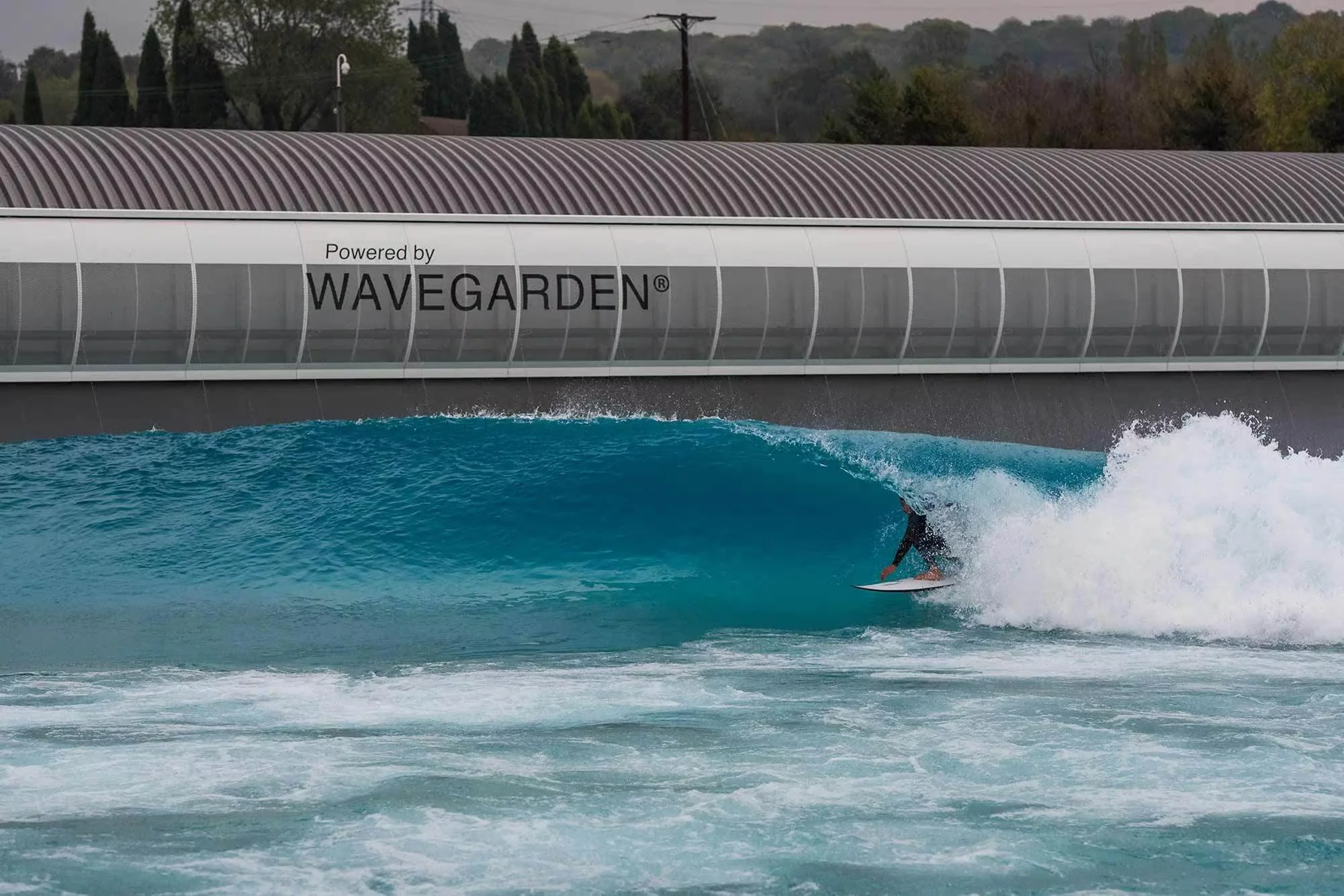 Un surfista cabalga una ola en una piscina de olas artificiales con el letrero 'Powered by Wavegarden' en la estructura.