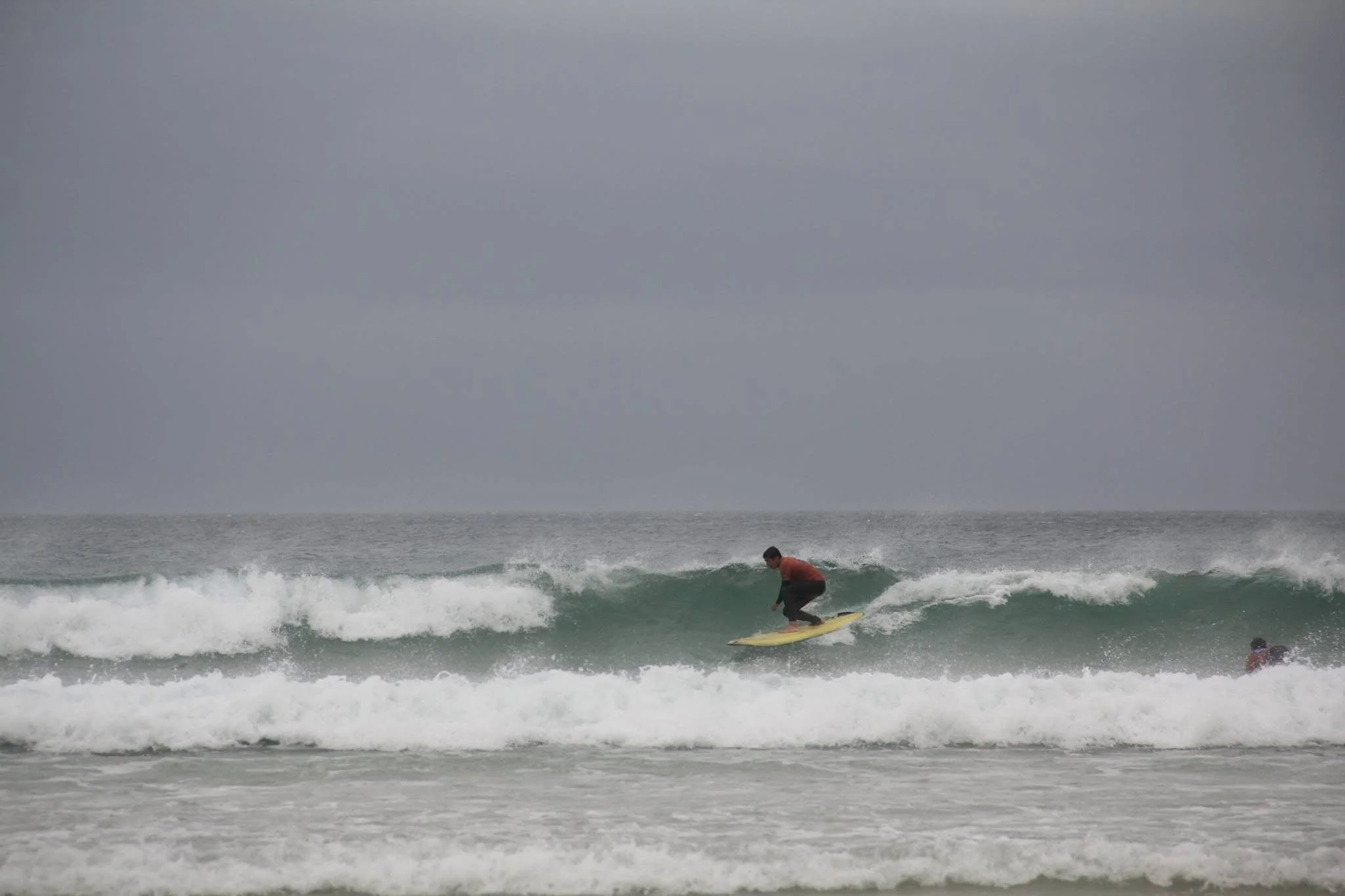 Joven surfeando en el océano, con olas y cielo nublado.
