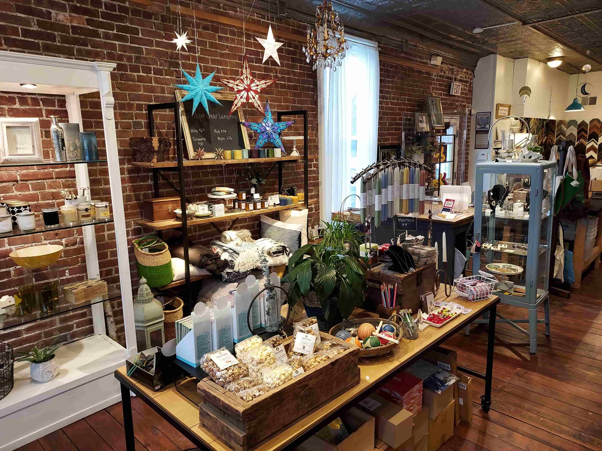 Boutique interior shot showing a bright window, layered shelving with curated gifts, and a mix of home decor and specialty items.