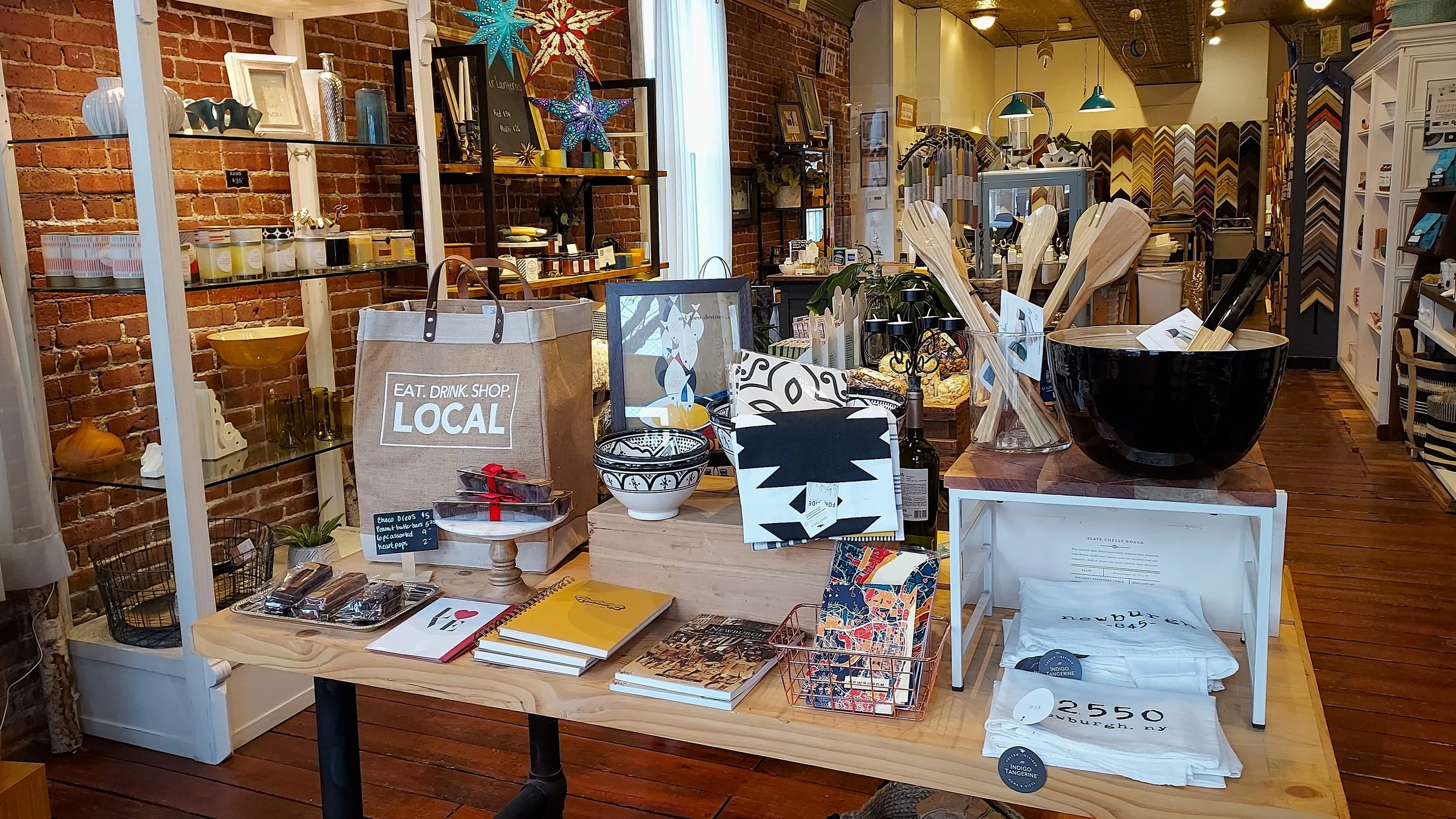 Retail display of unique artisan gifts, kitchen bowls, wooden spoons, and colorful notebooks in a boutique store.