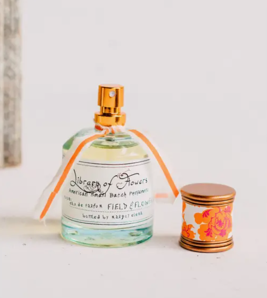 Library of Flowers Field & Flowers Parfum, a glass bottle with a gold sprayer and a patterned lid, tied with an orange ribbon.