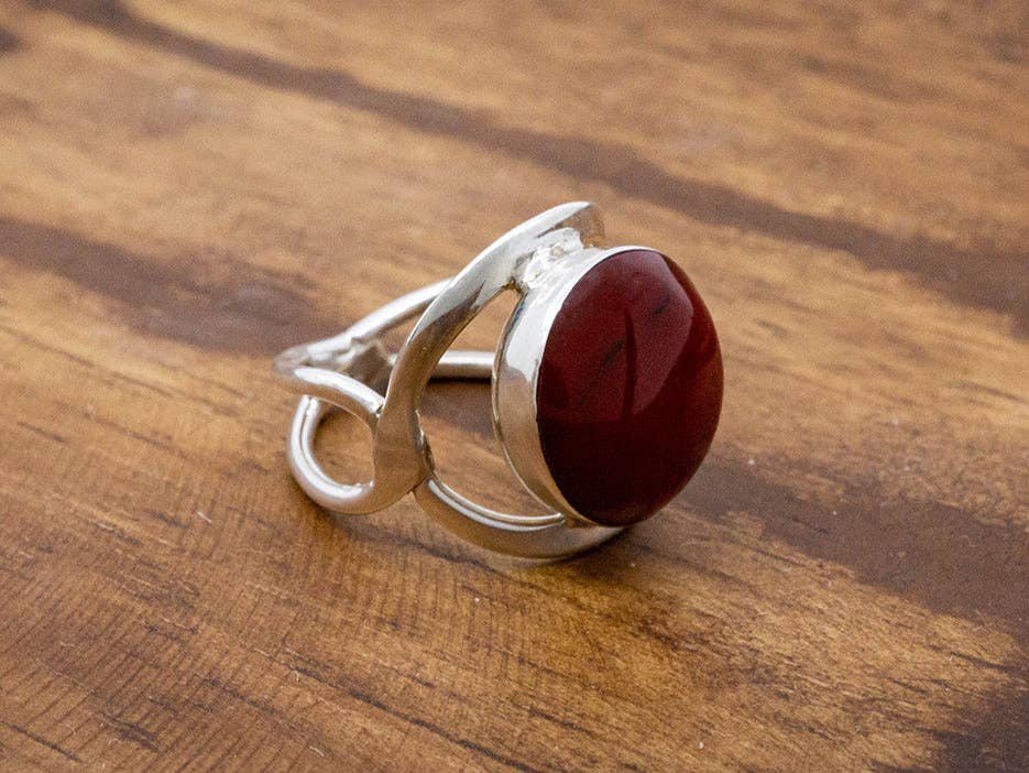 Corazon Red Jasper Sterling Silver Ring with an oval red stone set in a modern silver band on a wood surface.