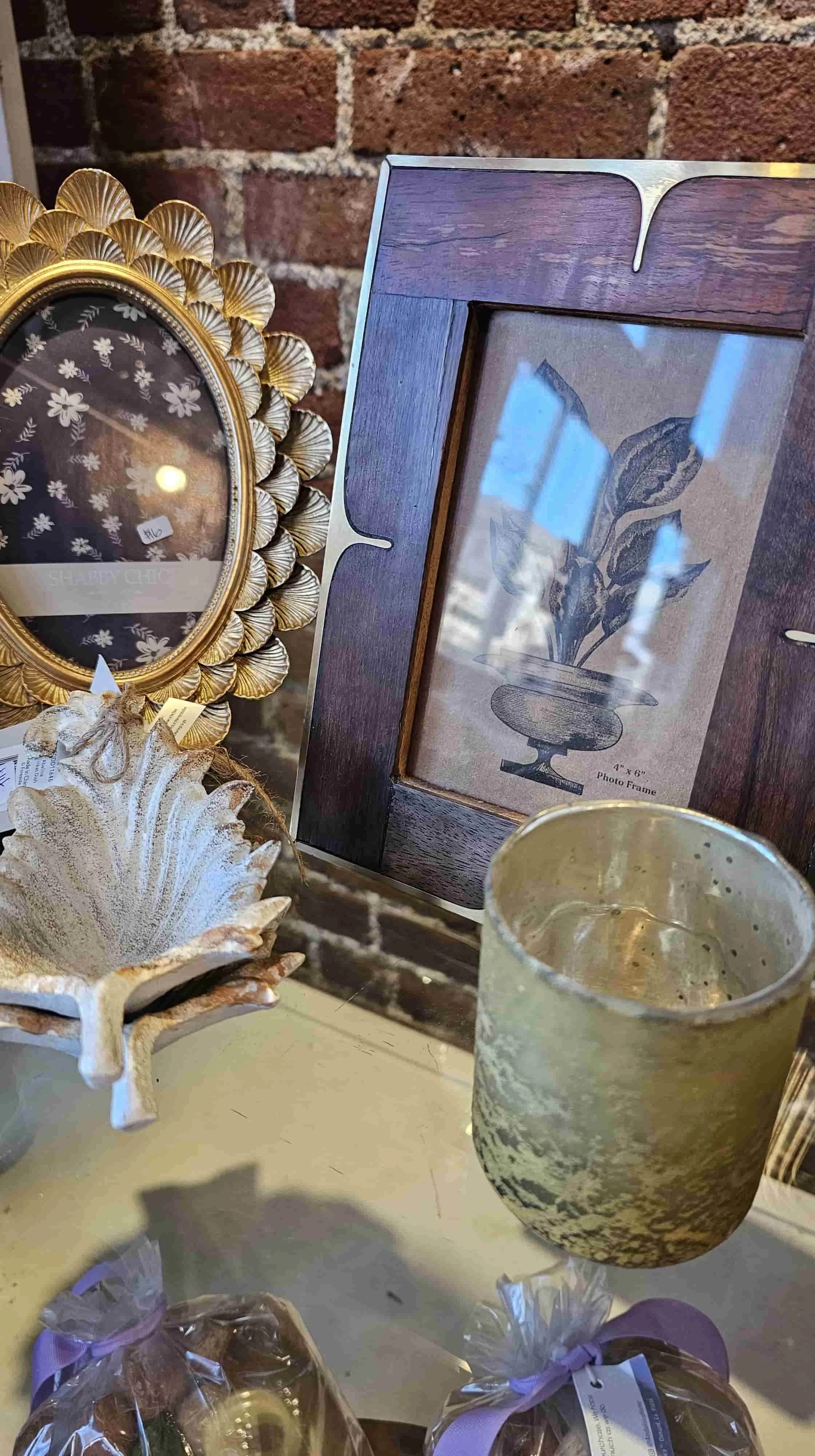 Ornate gold oval picture frame, wooden framed botanical print, and distressed seashell dish displayed on a shelf.