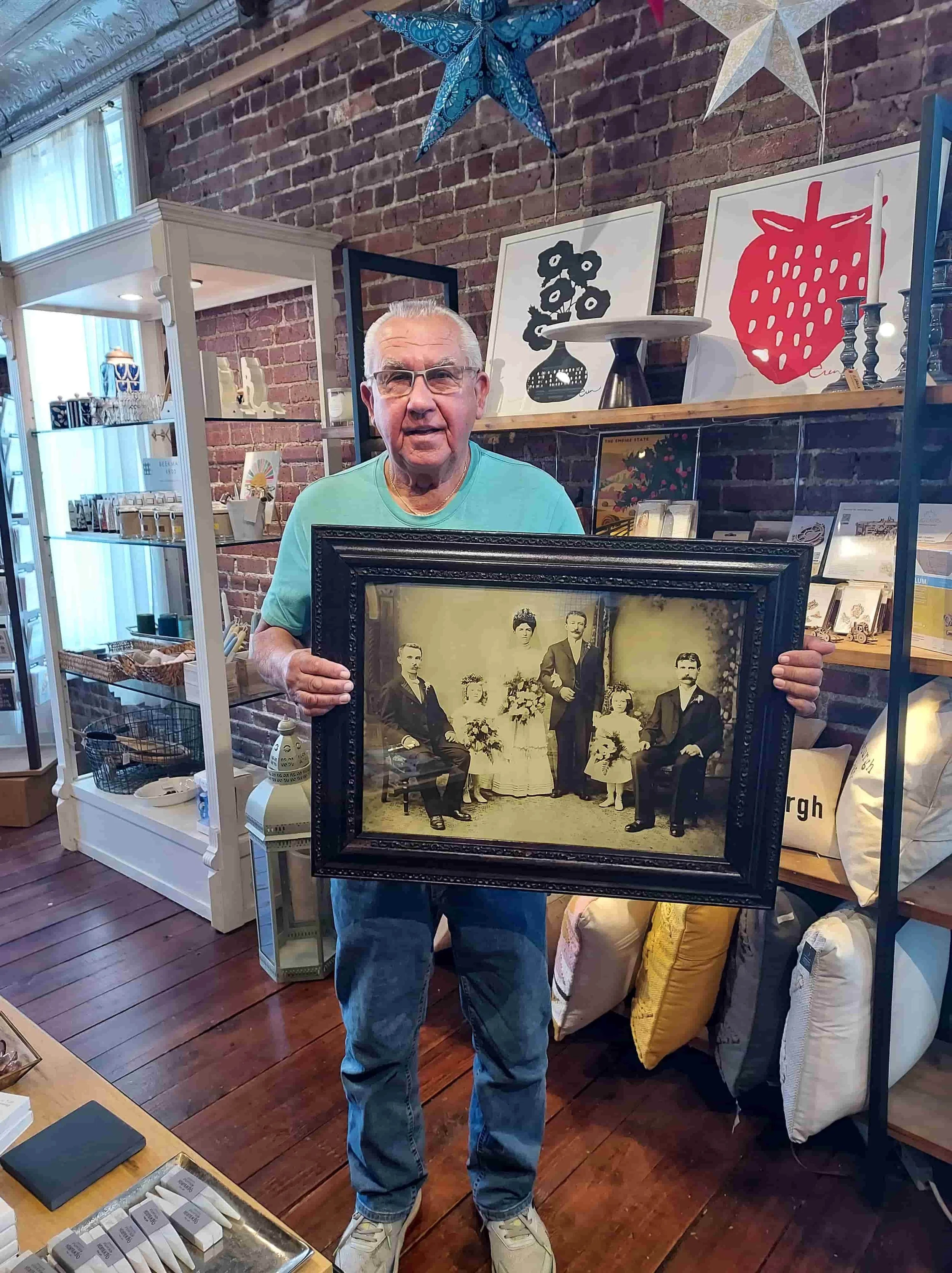 Happy client holding a newly restored and custom-framed antique family wedding photograph inside the Newburgh Mercantile gift shop.