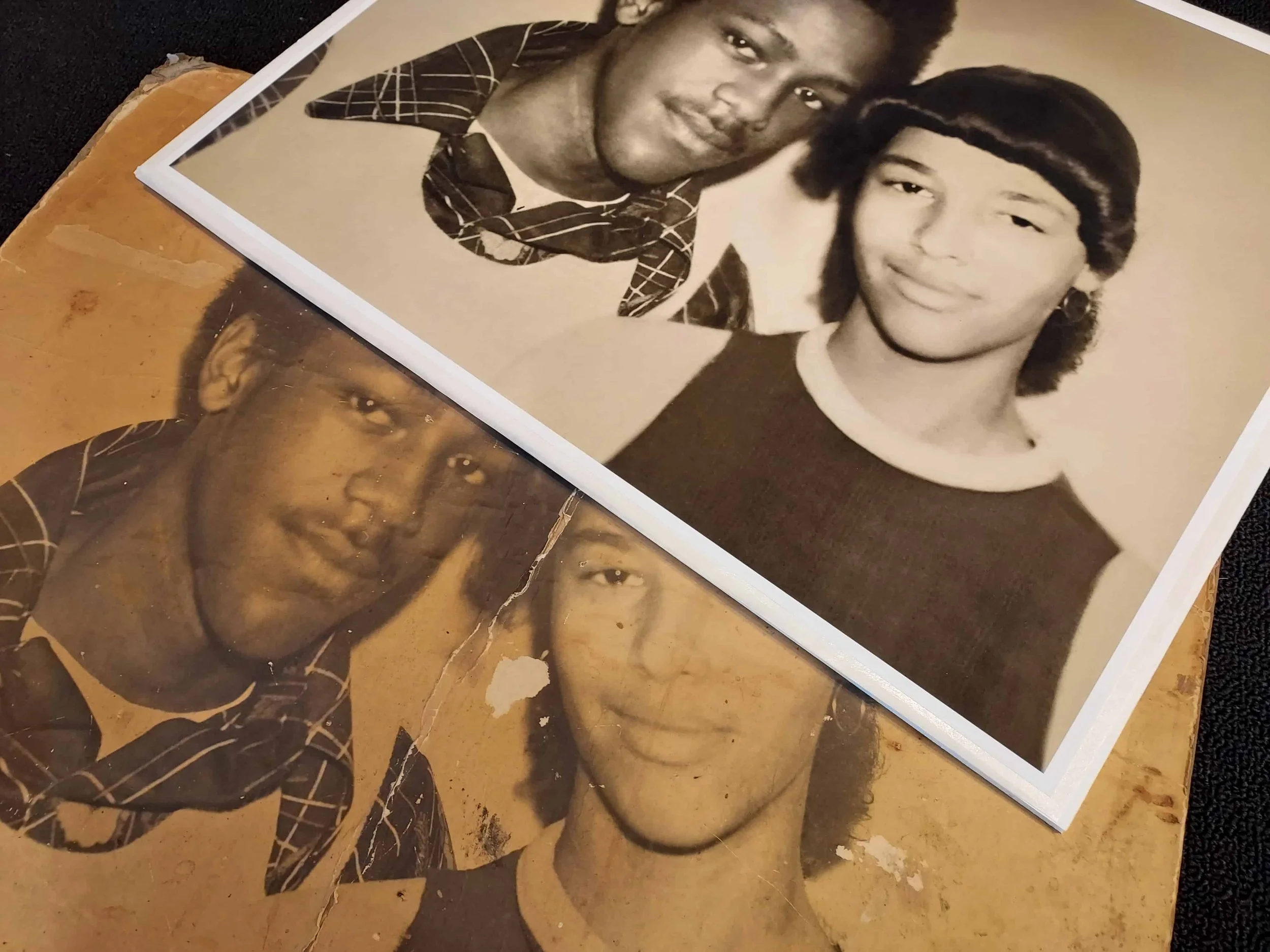 A new, restored print of two young people resting on top of the original, damaged vintage photograph. Photo restoration service offered by Newburgh Mercantile