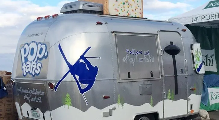 Silver popcorn trailer with a silhouette of a skier and the pop tarts logo, parked outdoors under a cloudy sky.