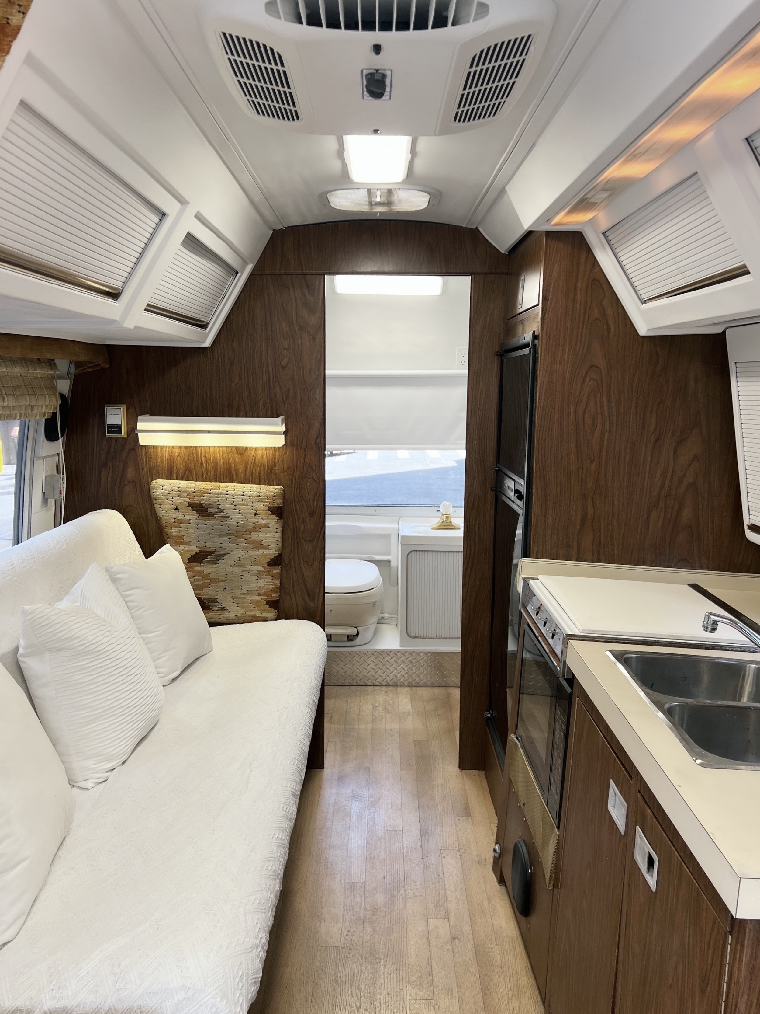 Interior of a compact RV with a futon sofa, kitchen area, and a bathroom with a toilet at the back.