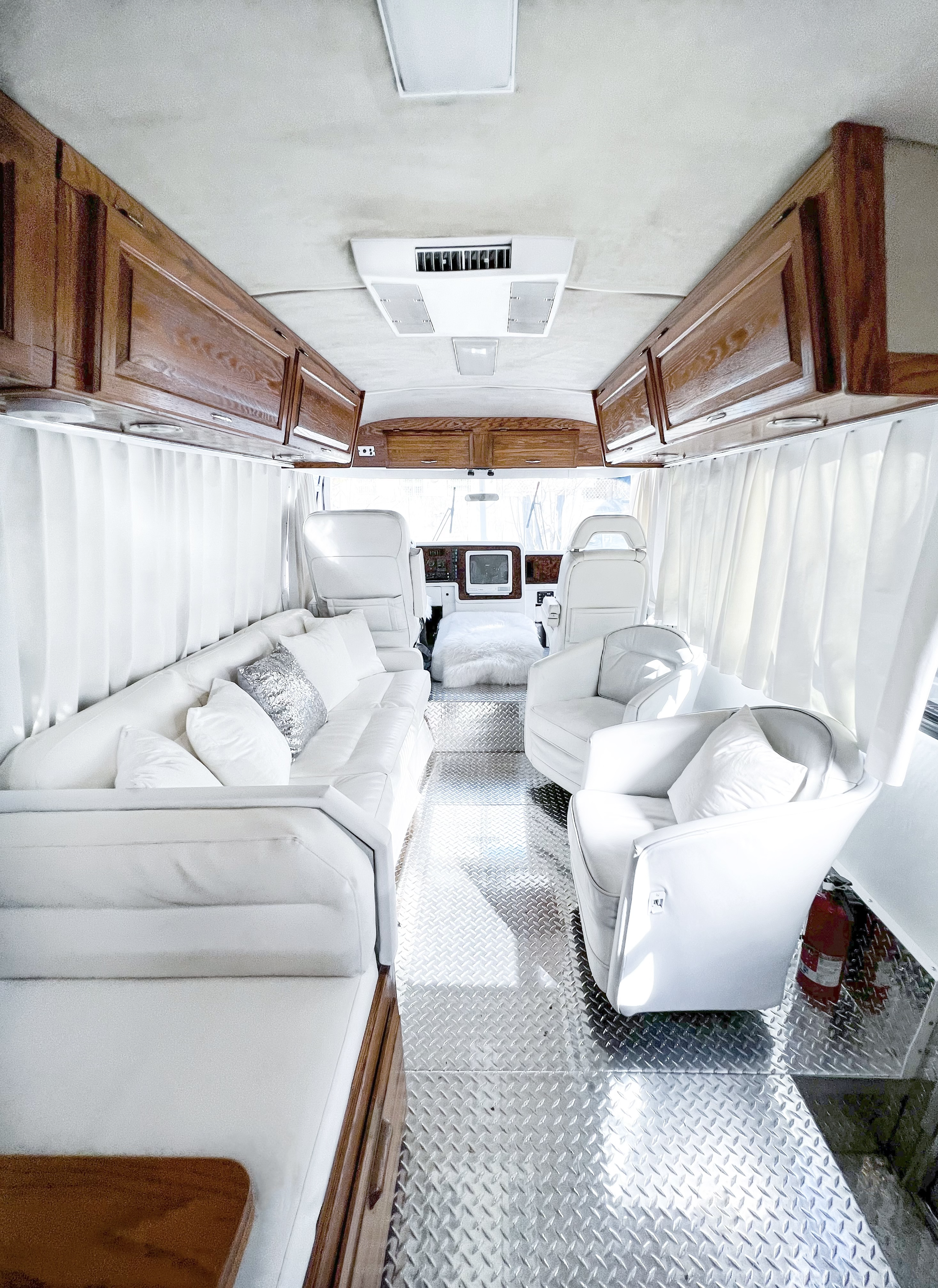 Interior of a luxury motorhome or yacht with white leather seating, wooden cabinetry, and aqua flooring.