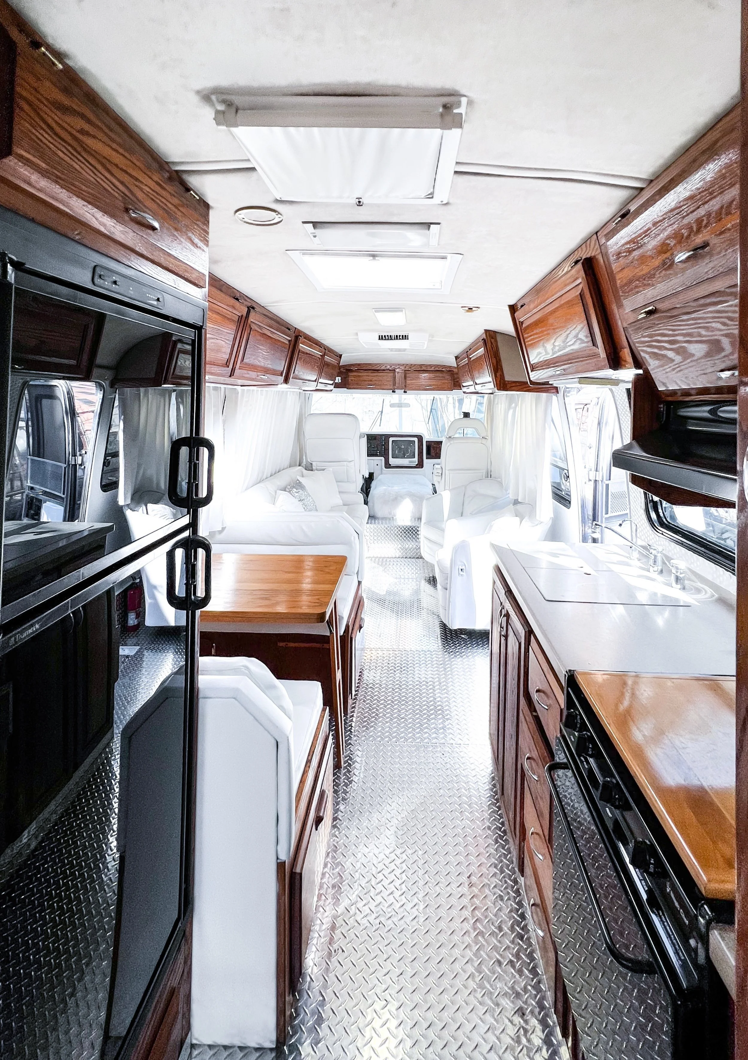 Interior of a boat or RV with wooden cabinets, white leather seating, a kitchen sink, and a small dining area with a table and chairs.