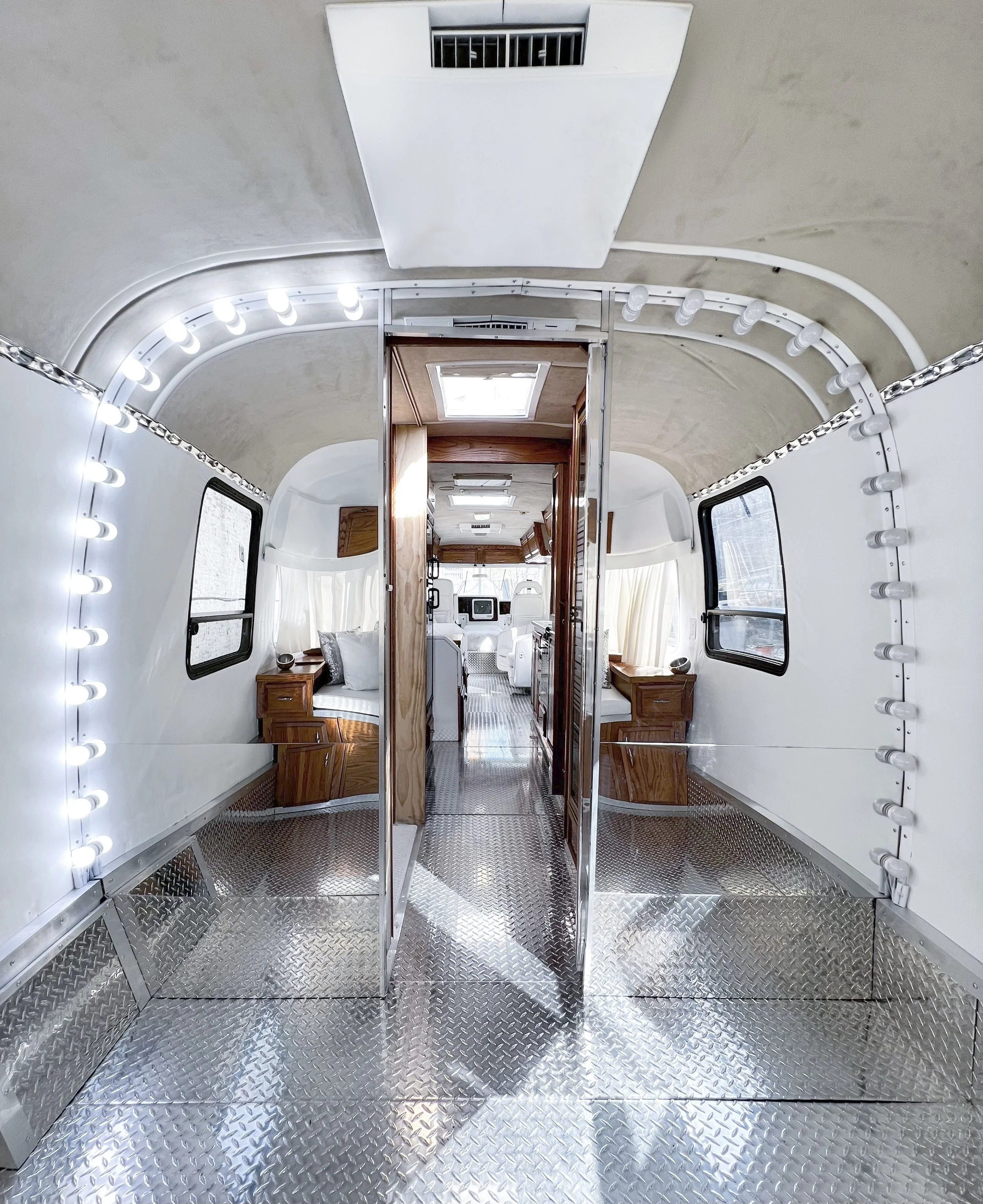 Interior view of a vintage camper or trailer with diamond plate flooring, wooden accents, and two side seating areas with windows.