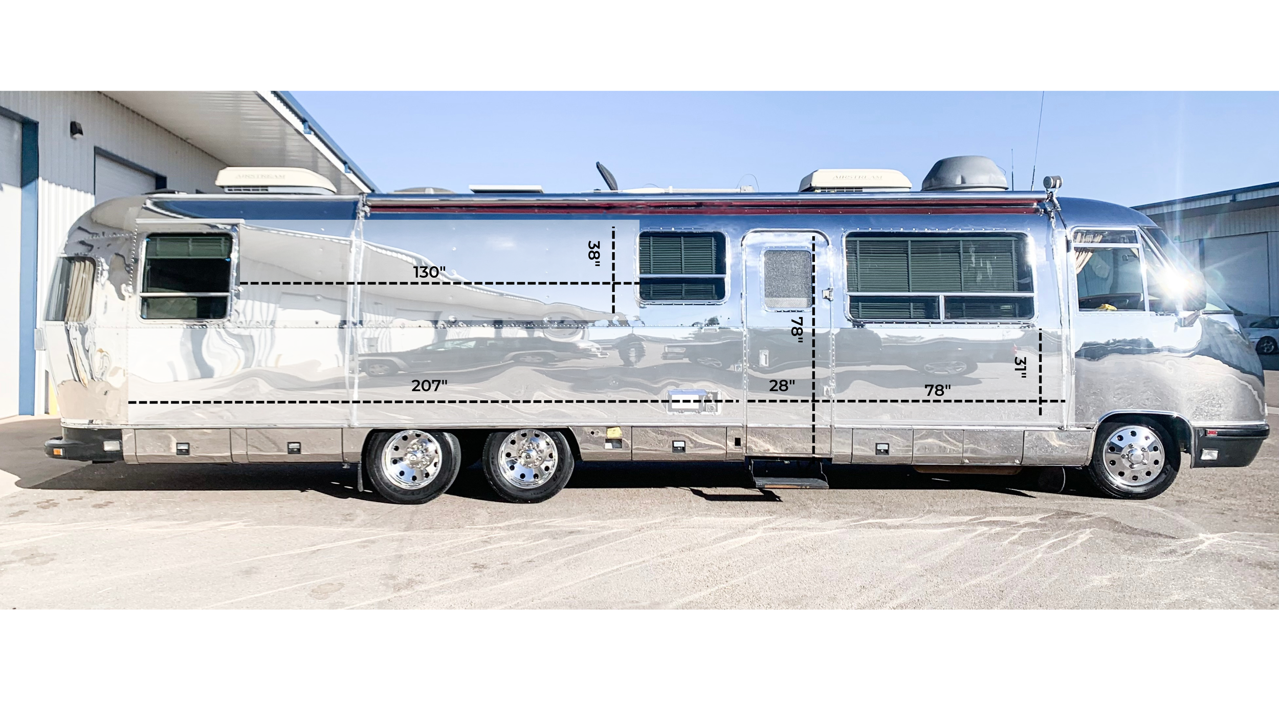 Side view of a shiny silver Airstream travel trailer with measurements marked, parked outdoors near a light-colored building, under a clear blue sky.