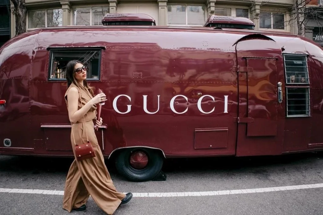 A stylish woman walks past Gucci’s burgundy Airstream parked outside the brand’s SoHo flagship. The polished trailer doubles as a mobile coffee pop-up, drawing crowds and embodying Gucci’s modern take on luxury street experiences.