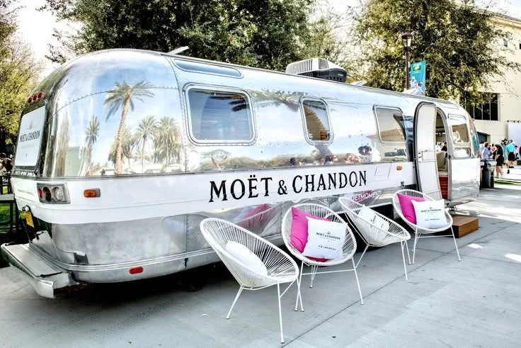 A polished Moët & Chandon Airstream transformed into a luxury outdoor lounge, featuring modern seating and a chic champagne experience under the palms.