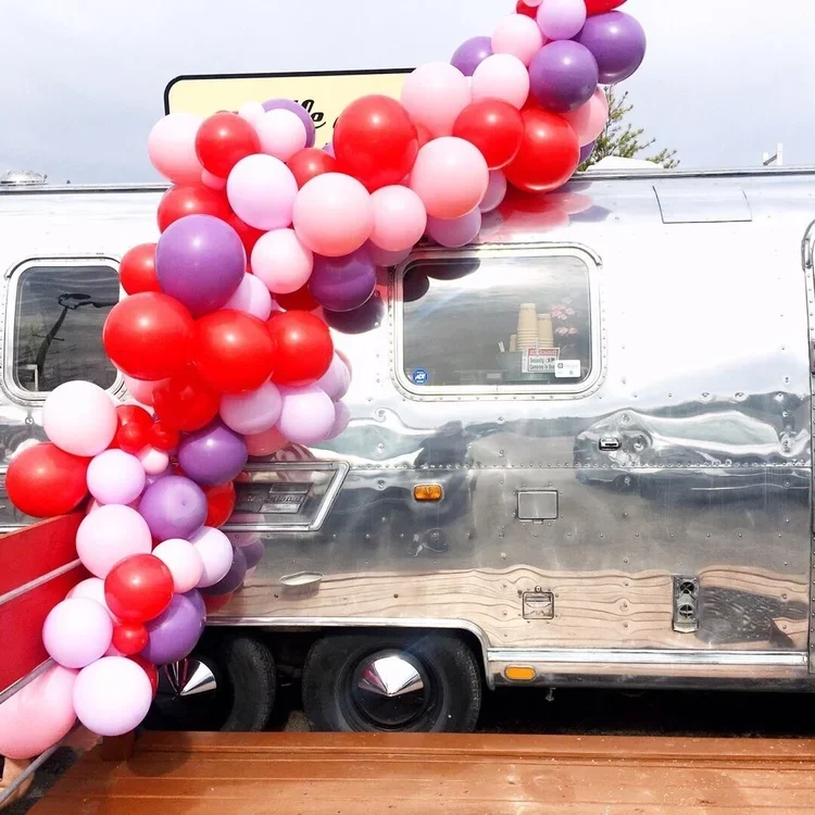 Decorative red, pink, and purple balloons arranged on a silver trailer with a wooden surface in front.