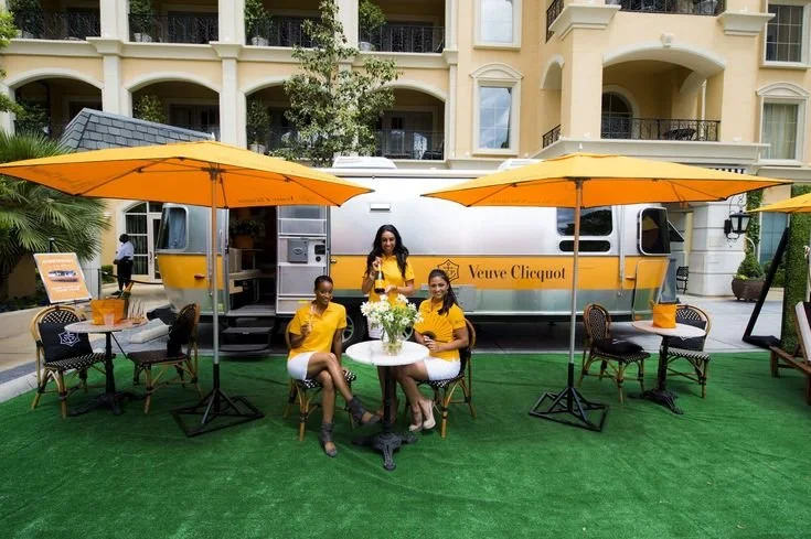 A sleek Veuve Clicquot Airstream transformed into an outdoor champagne bar, complete with yellow parasols, elegant seating, and a luxury garden ambiance.