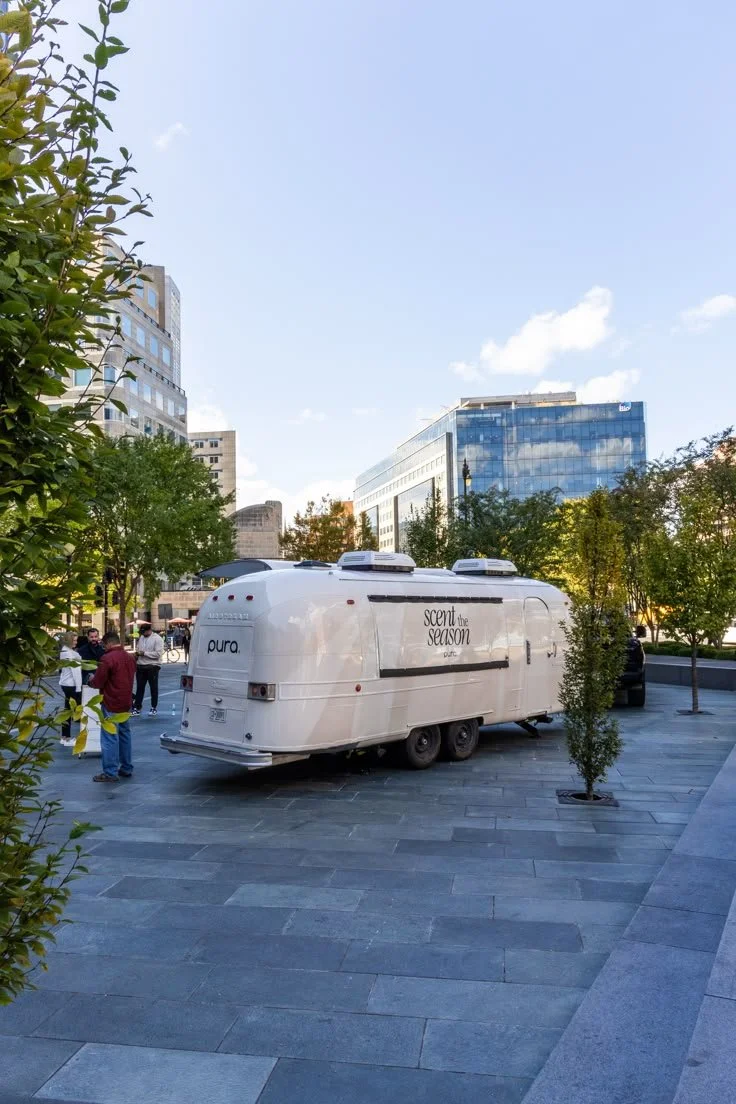 A white Pura Airstream pop-up activation in a modern NYC plaza, promoting the “Scent the Season” campaign with a sleek, minimalist design.