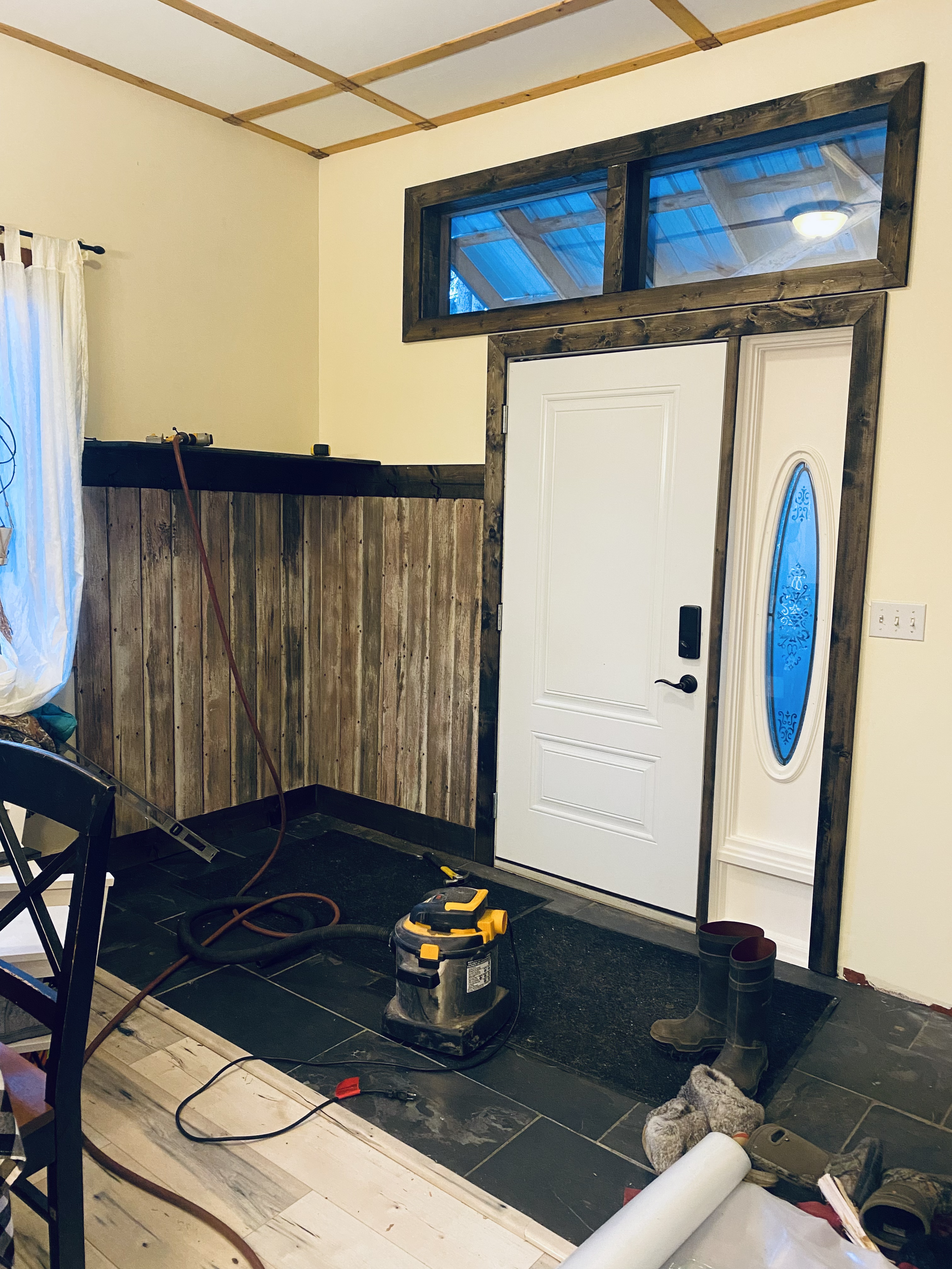 Interior of a house entryway and door under renovation, with construction tools, boots, and materials on the floor.