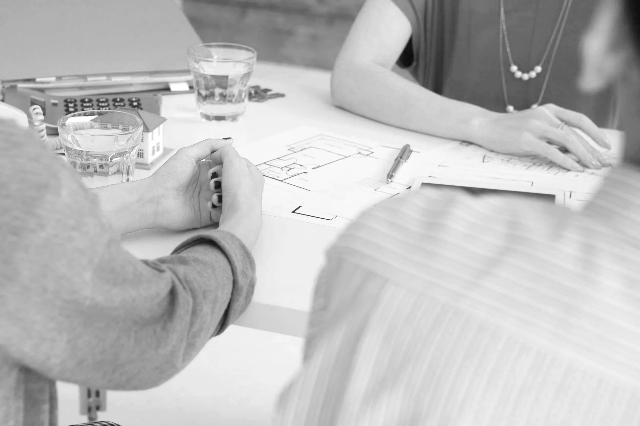 People sitting at a table with architectural blueprints, glasses of water, and office supplies during a meeting.